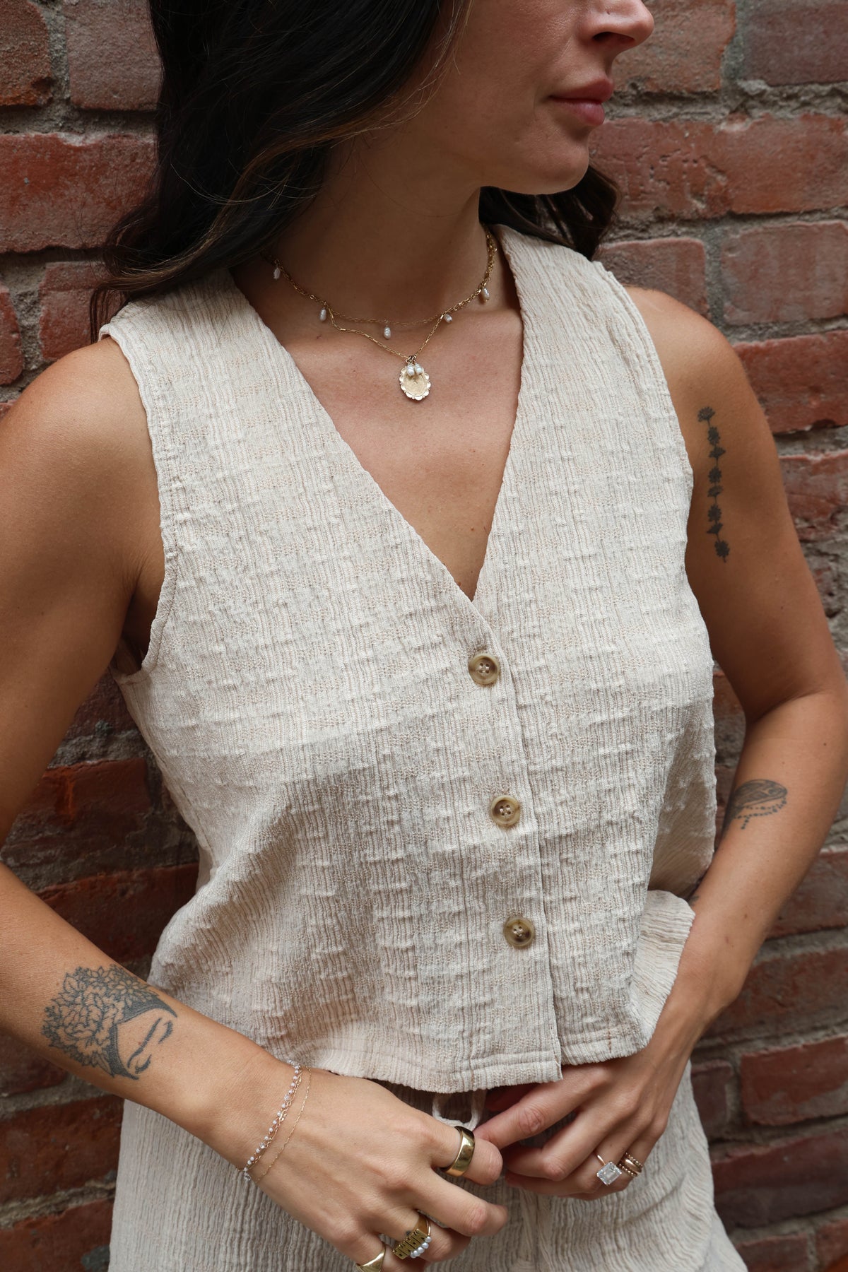 Woman wearing a beige jumpsuit standing against a brick wall.