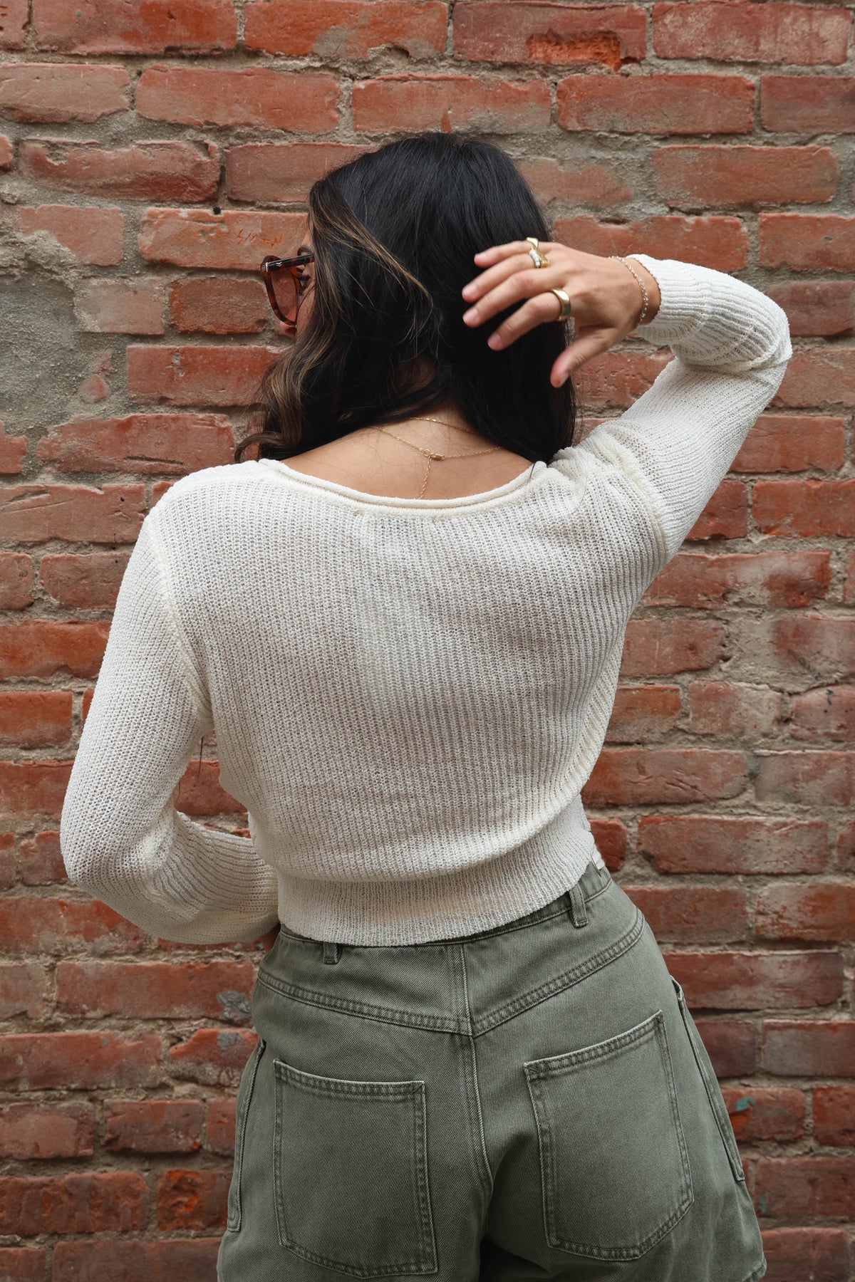Person wearing a white sweater and green pants against a brick wall.
