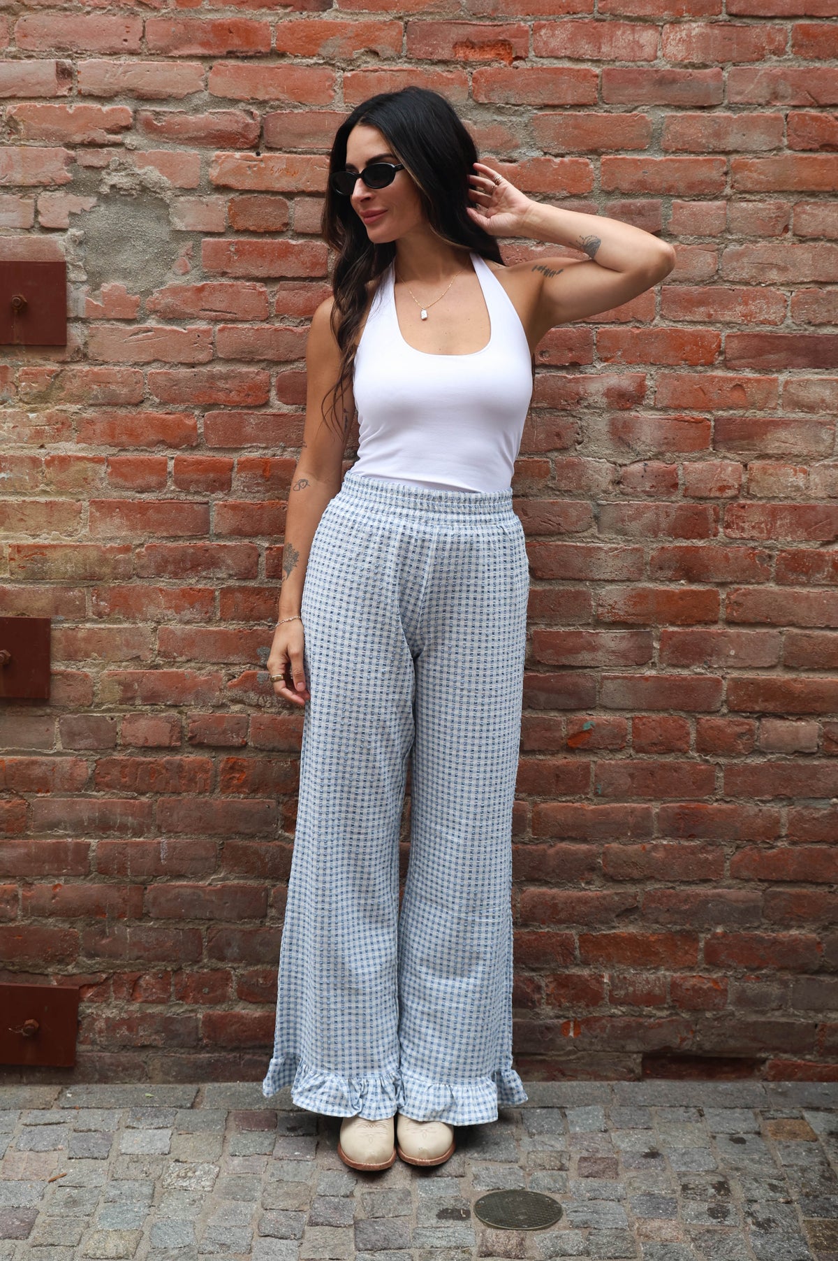 Woman wearing a white top and checkered pants standing against a brick wall.