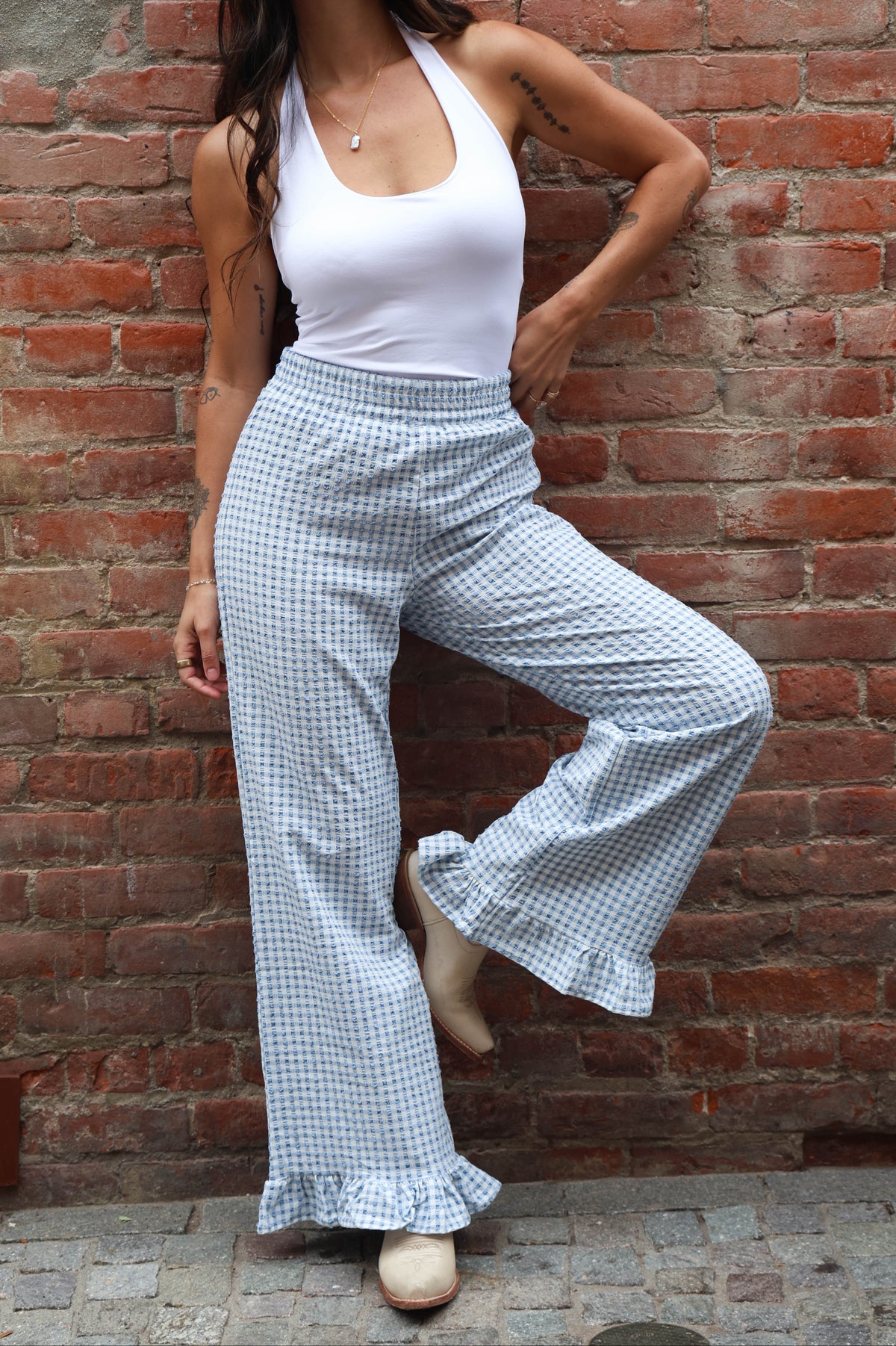 Woman wearing a white top and checkered pants against a brick wall.