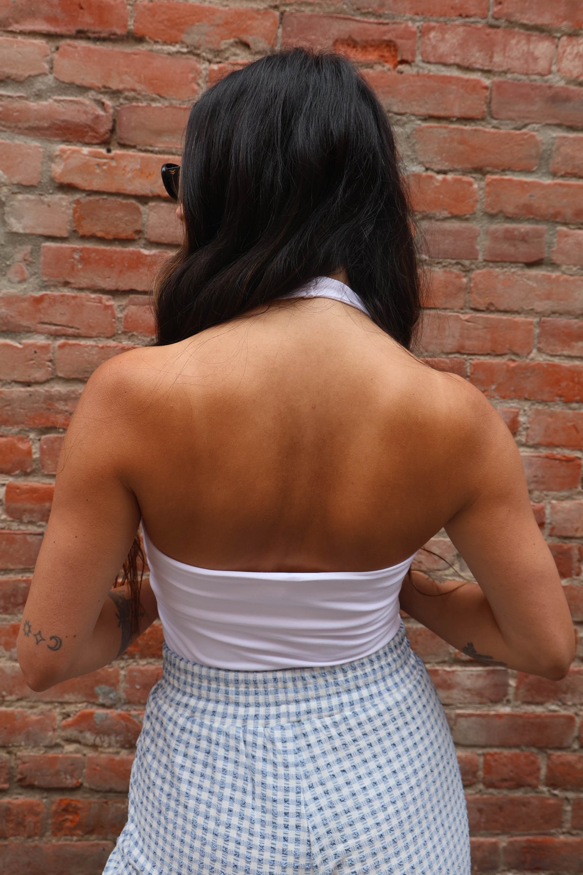 Person wearing a white top and checkered skirt against a brick wall
