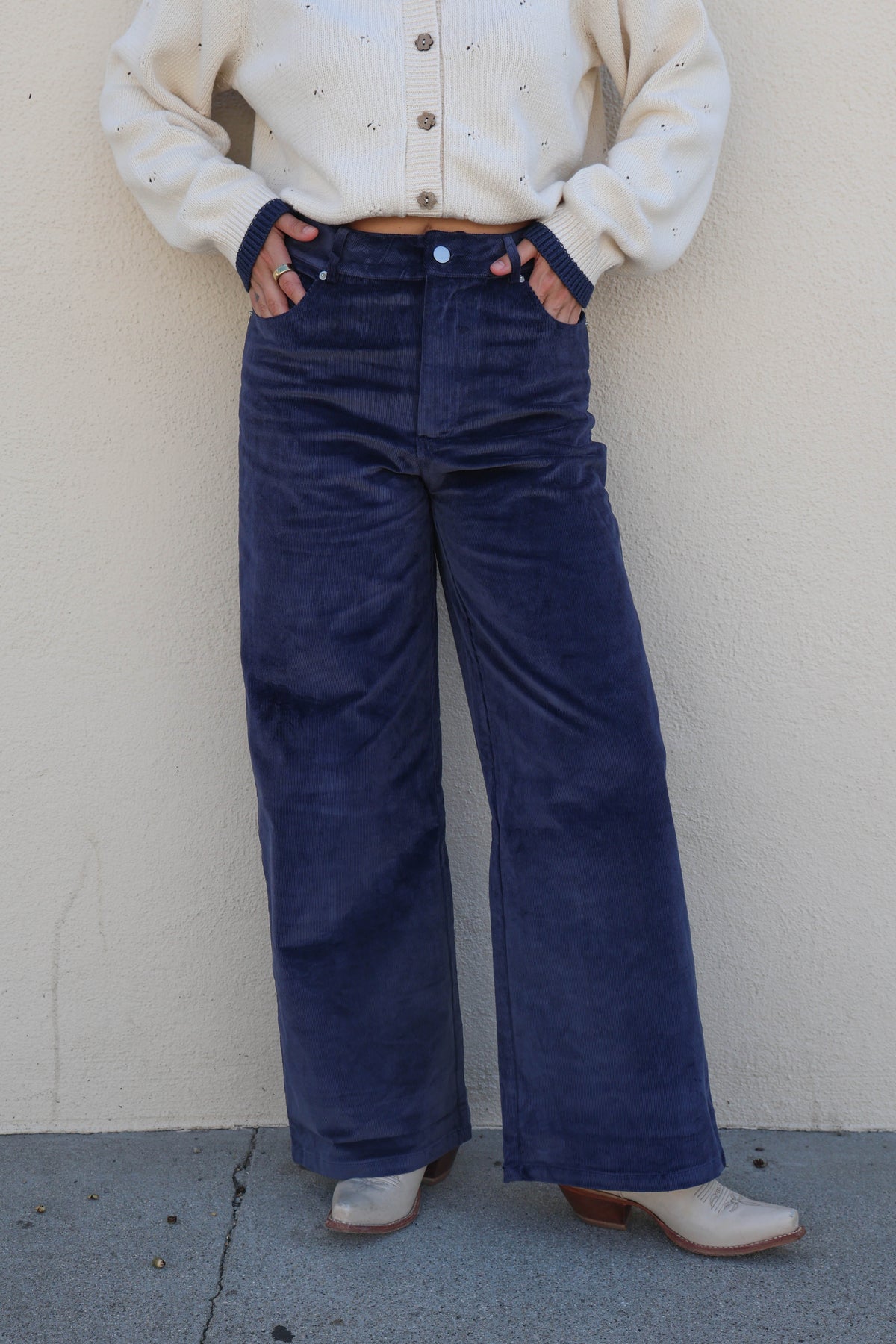 Woman modeling a pair of blue corduroy pants against a plain wall.
