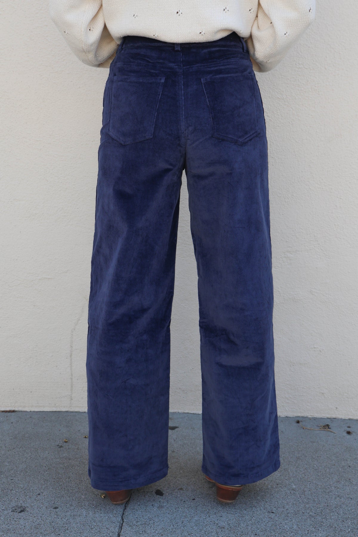 Woman modeling a pair of blue corduroy pants against a plain wall.