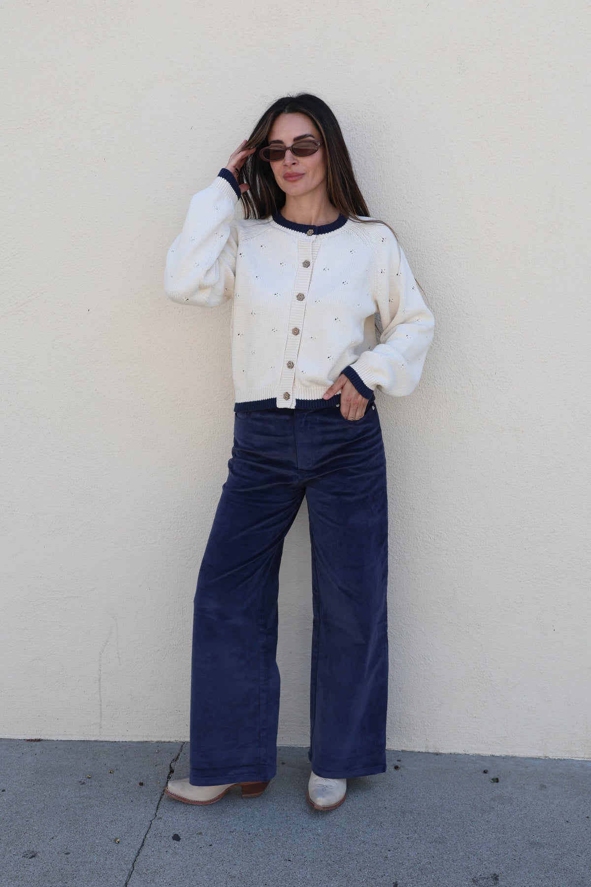 Woman modeling a pair of blue corduroy pants against a plain wall.