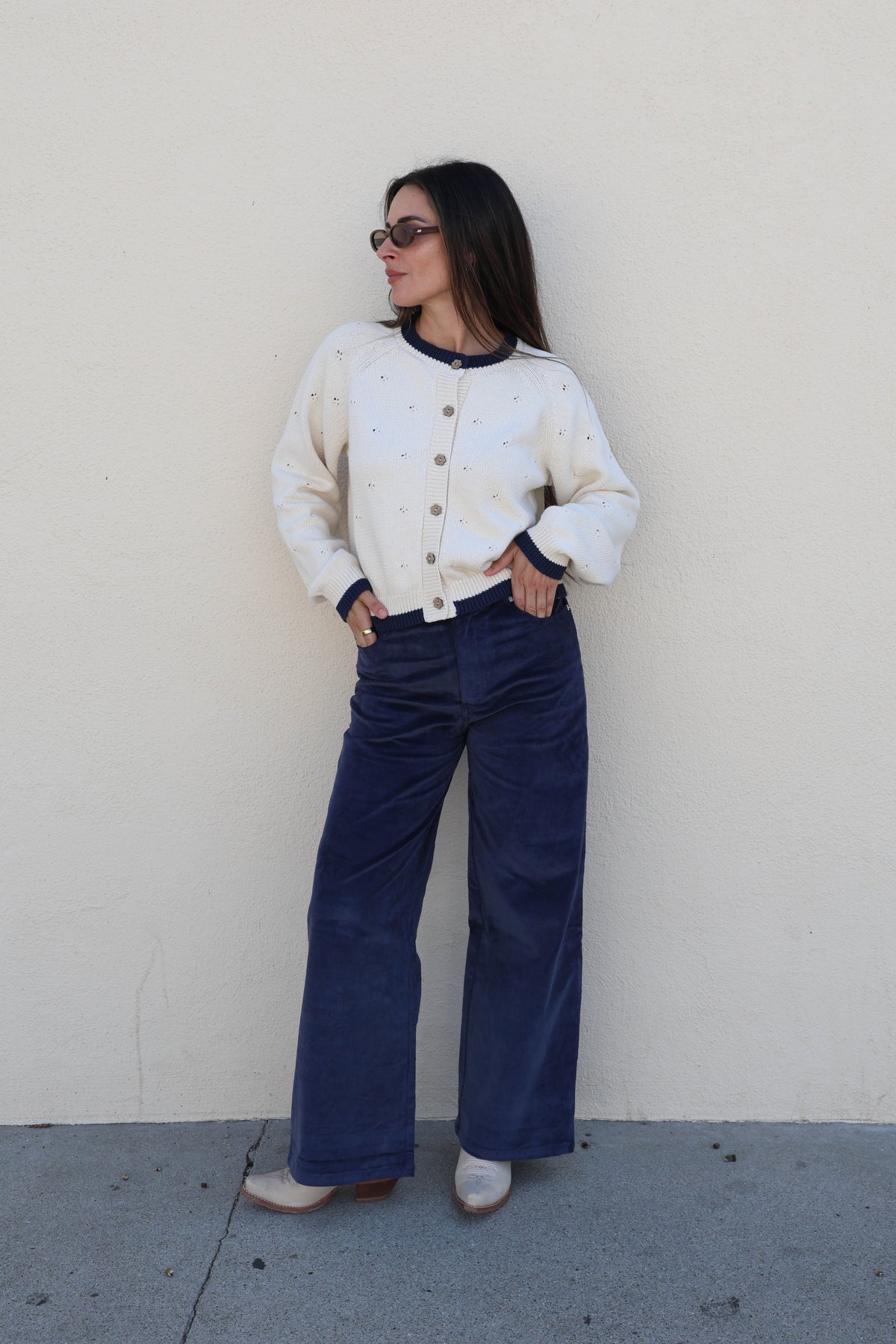 Woman modeling a pair of blue corduroy pants against a plain wall.