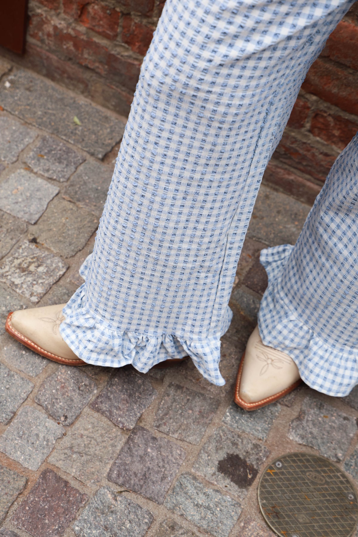Blue checkered pants with ruffled cuffs on a stone pavement.