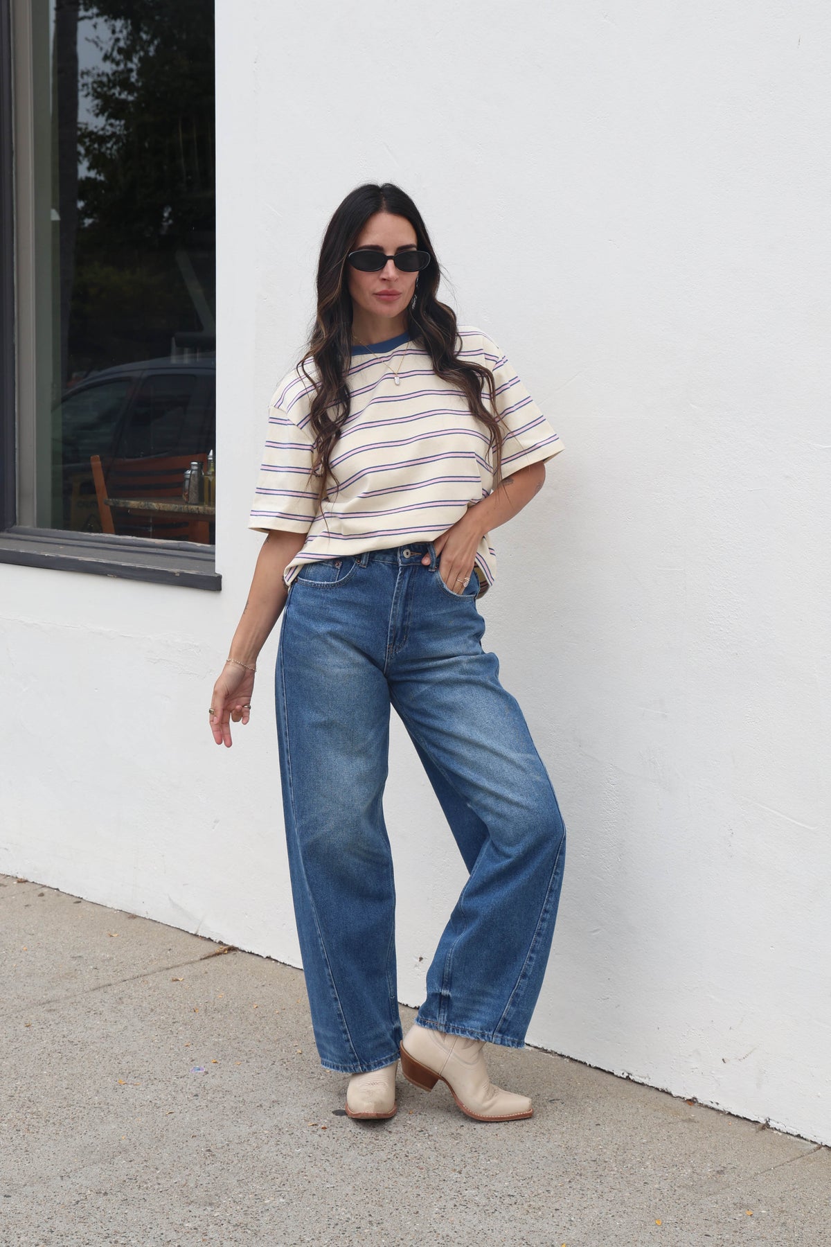 Woman wearing a striped shirt and blue jeans standing against a white wall.
