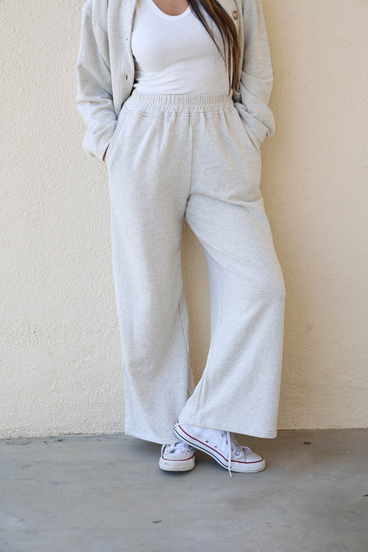 Woman wearing grey sweatpants against a plain wall.