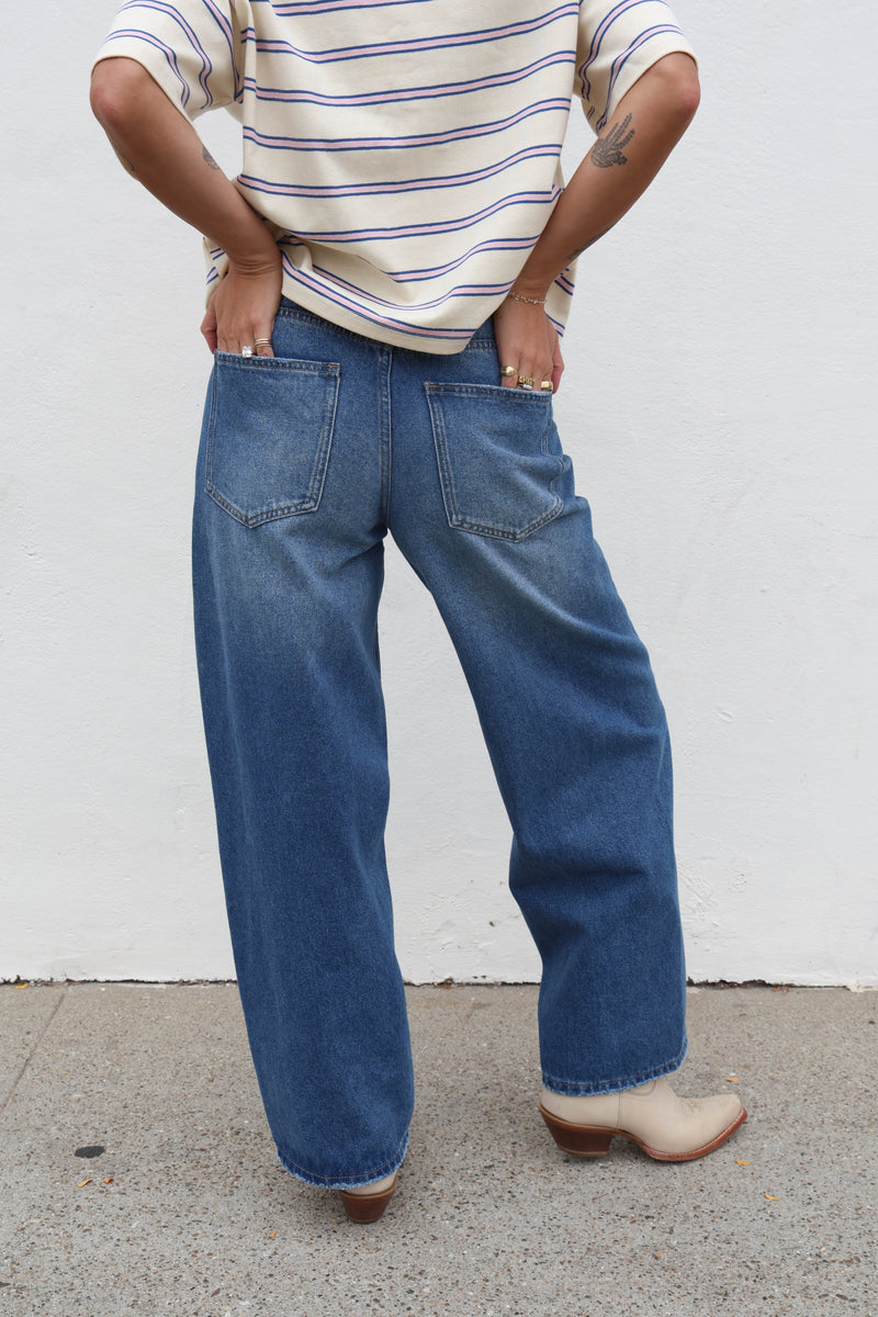 Person wearing blue jeans and a striped shirt against a white wall.