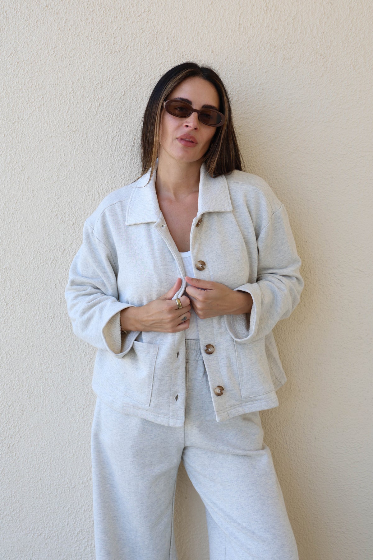 Woman wearing a grey sweat jacket against a plain wall.