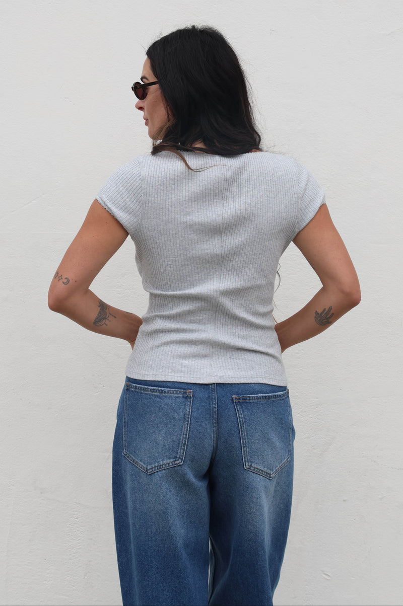 Person wearing a light gray sweater and blue jeans against a plain background