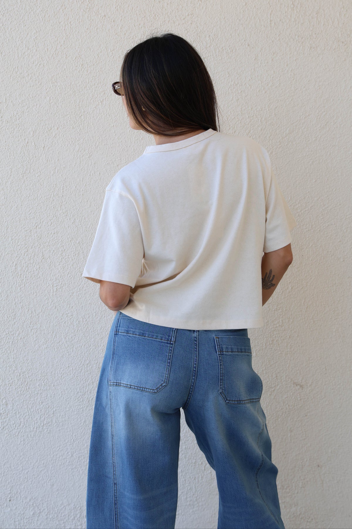 Woman wearing a plain tee and jeans against a plain wall.