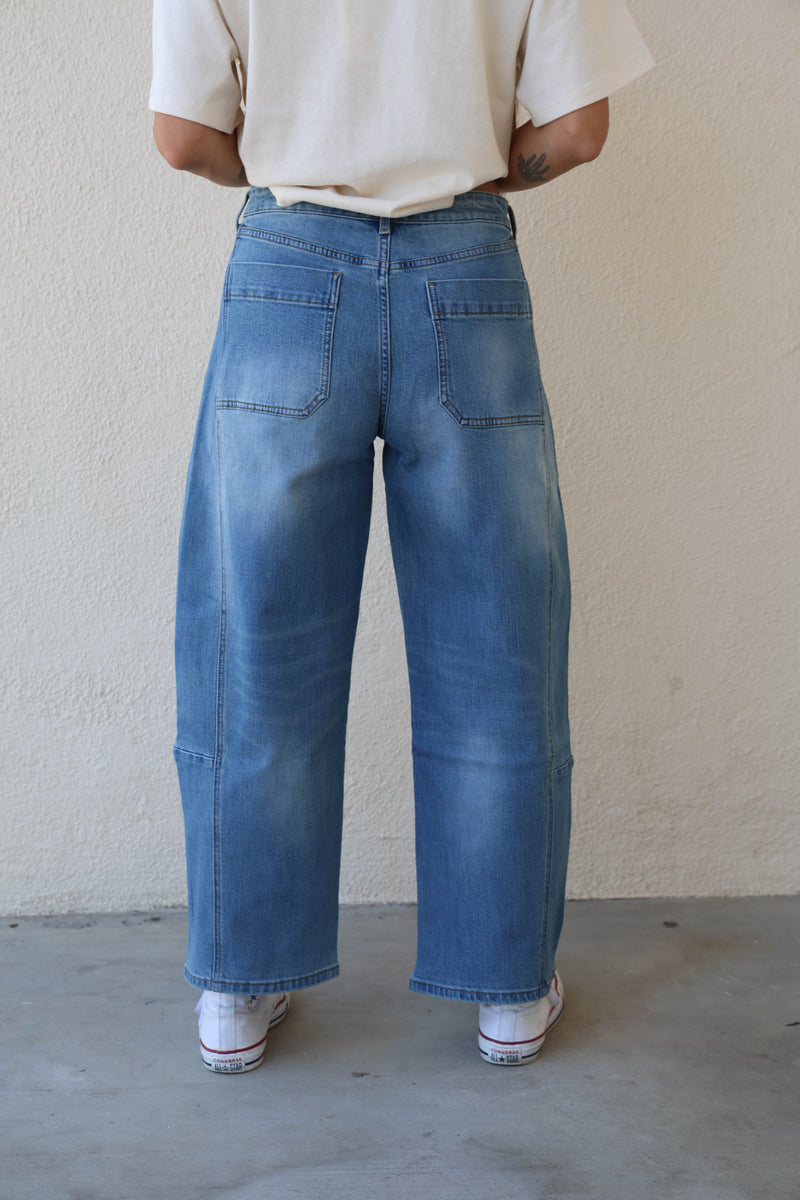 Woman modeling a pair of barrel jeans against a plain background.