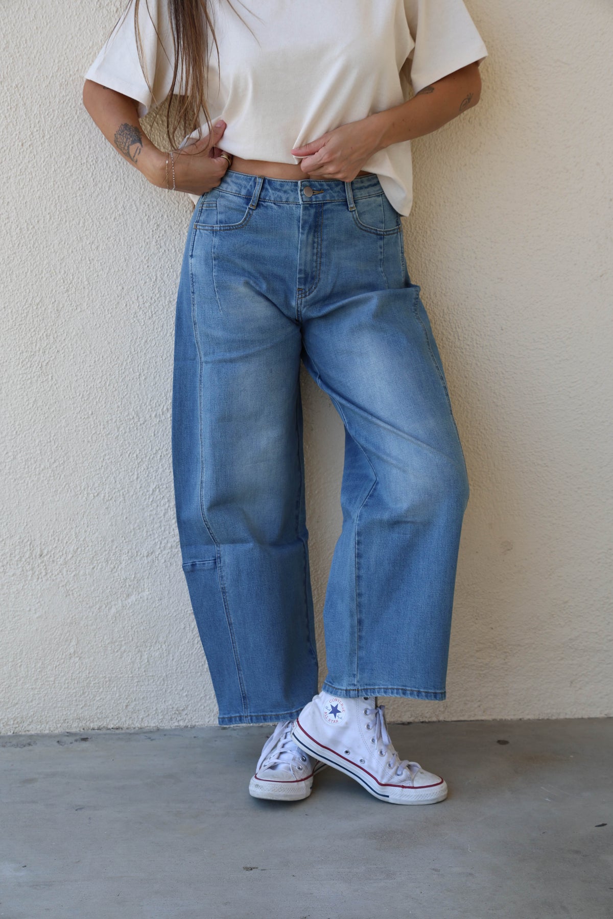 Woman modeling a pair of barrel jeans against a plain background.