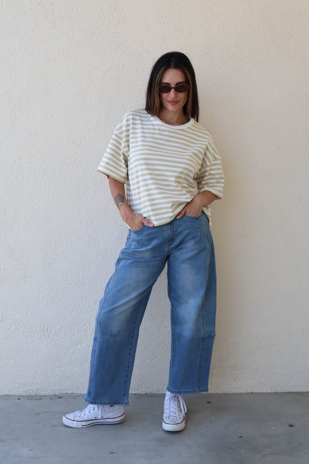 Woman wearing a striped tee with jeans against a plain wall.