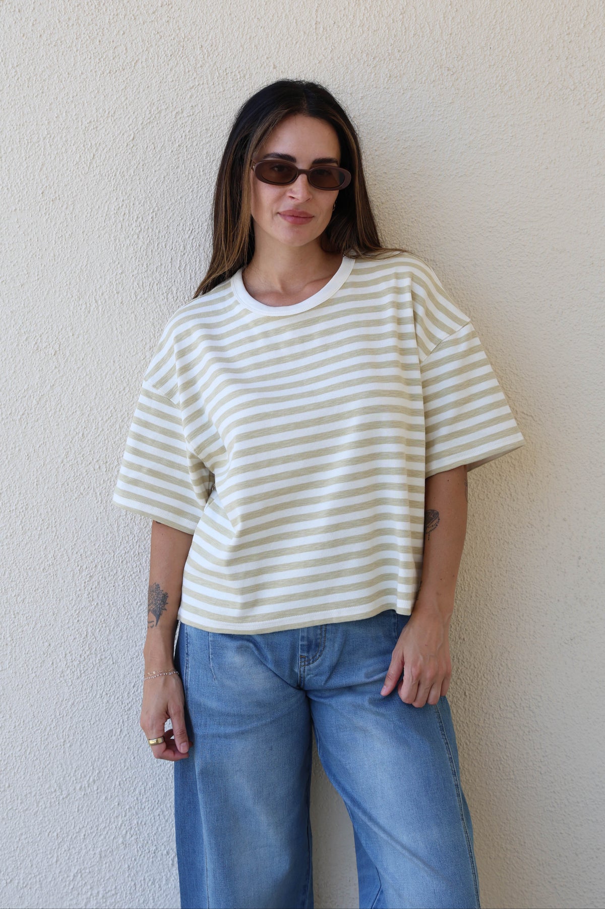 Woman wearing a striped tee with jeans against a plain wall.