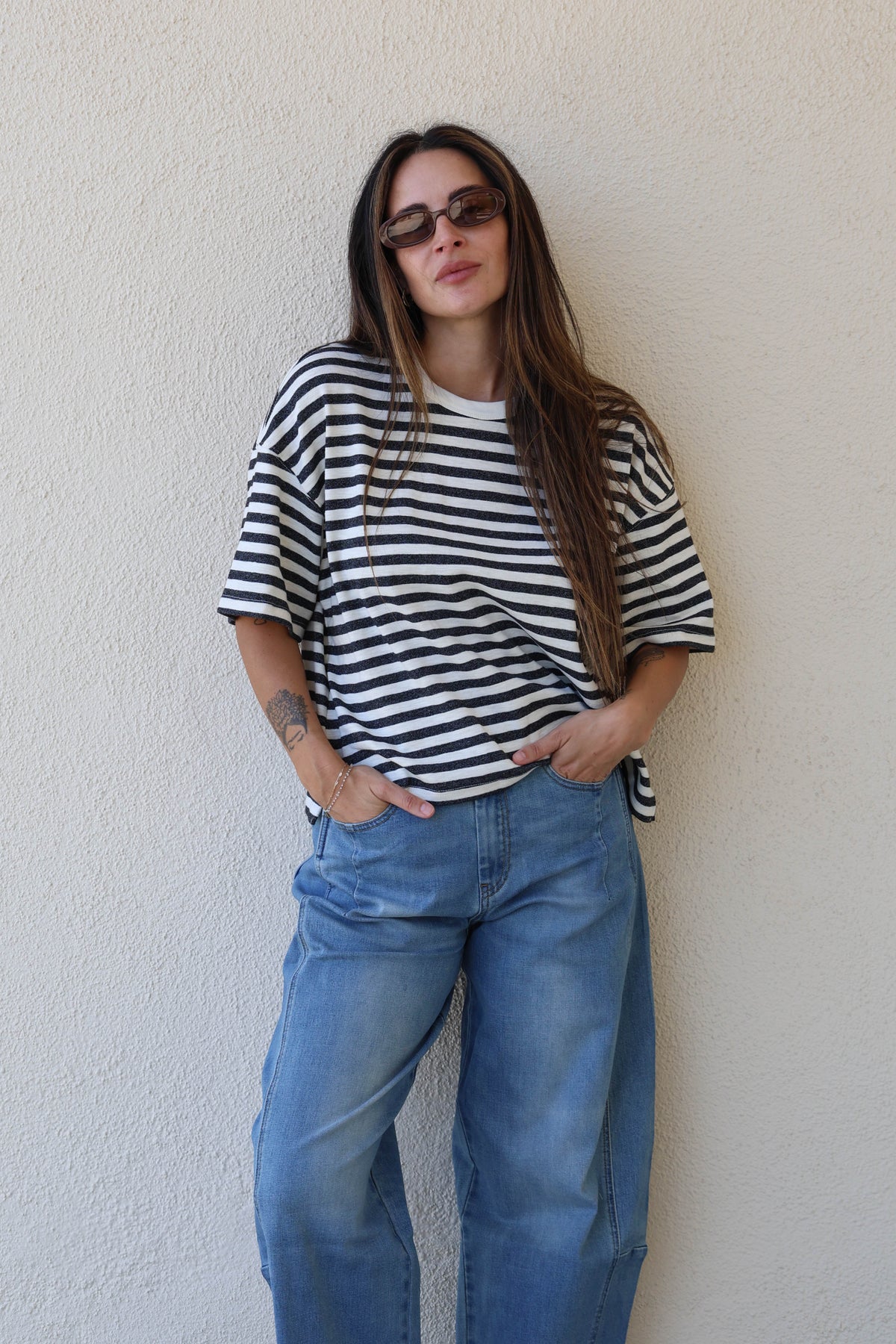 Woman wearing a striped tee and jeans against a plain wall.