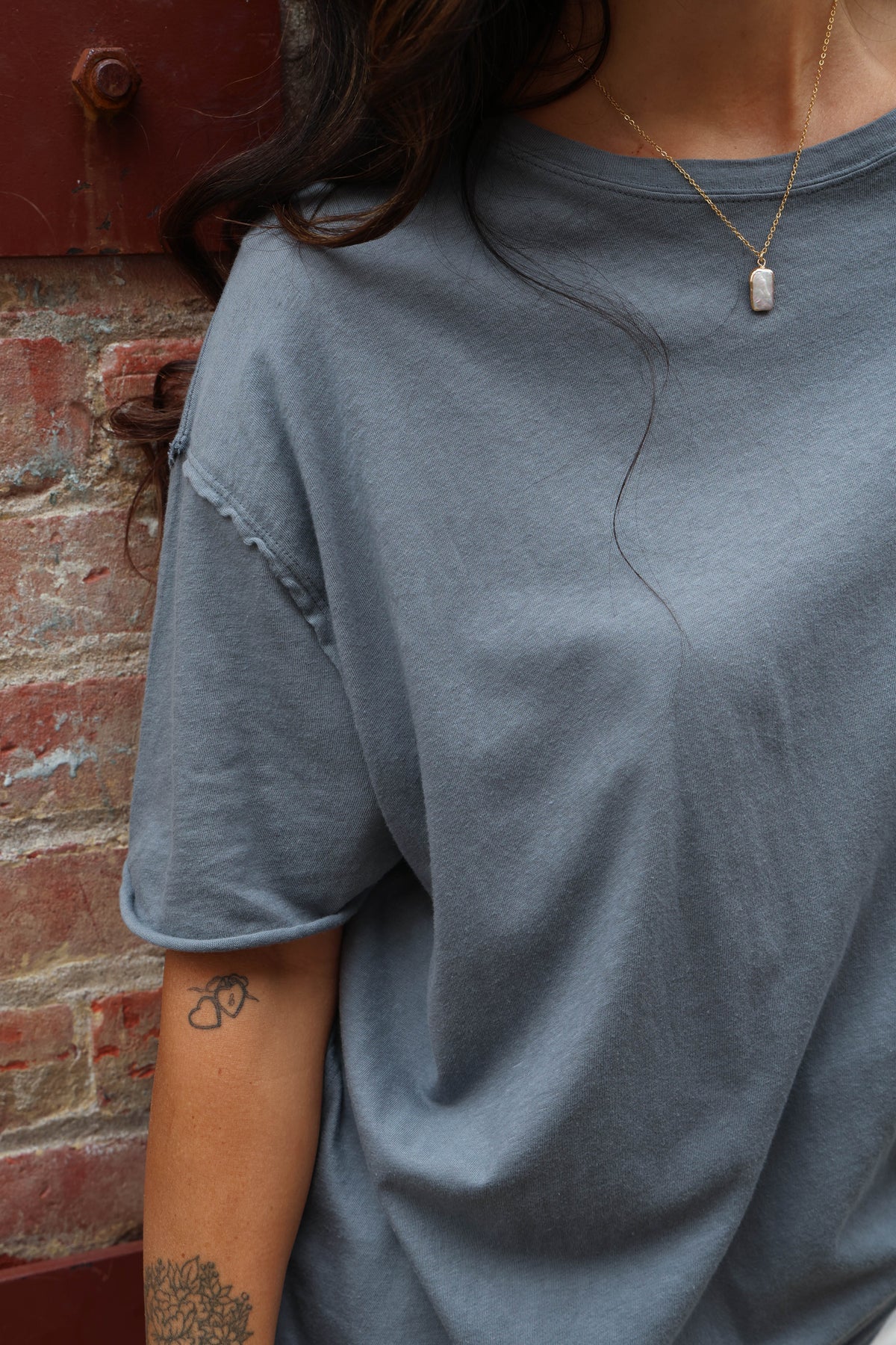 Person wearing a gray t-shirt with a red brick wall background