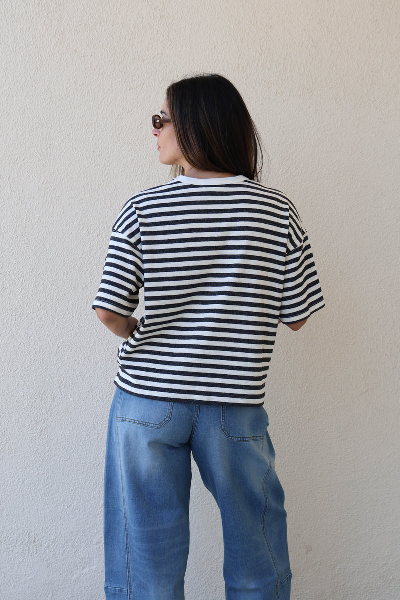 Woman wearing a striped tee and jeans against a plain wall.