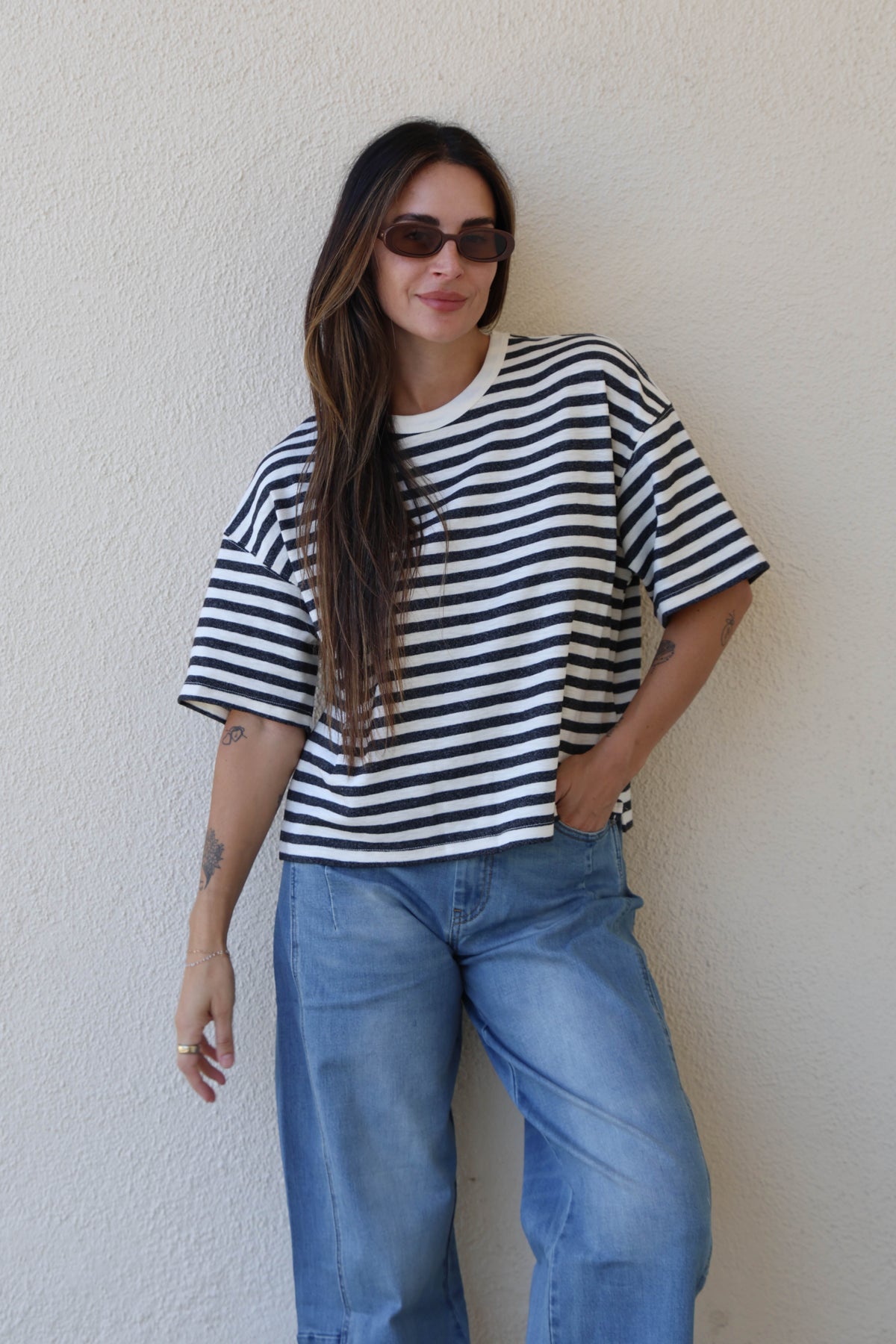 Woman wearing a striped tee and jeans against a plain wall.