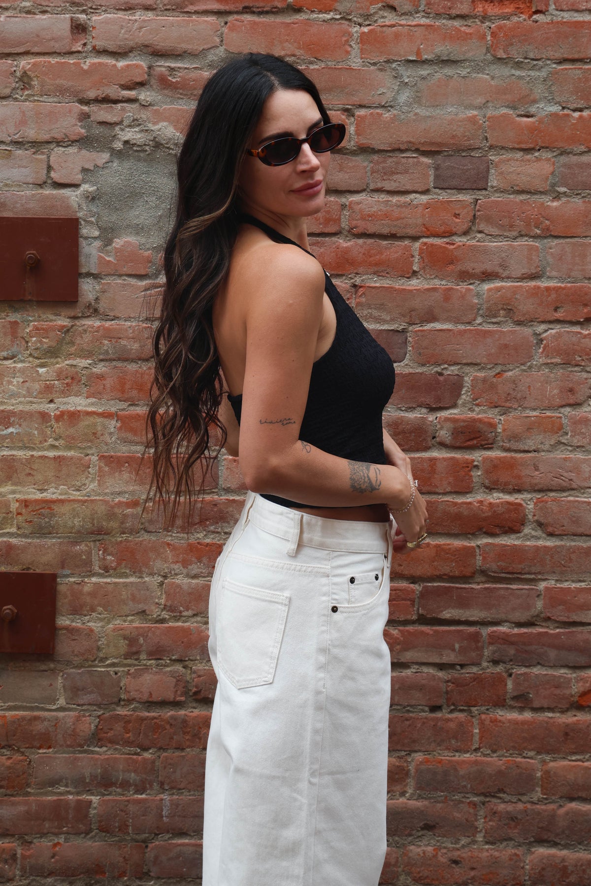 Woman wearing a black top and white pants against a brick wall