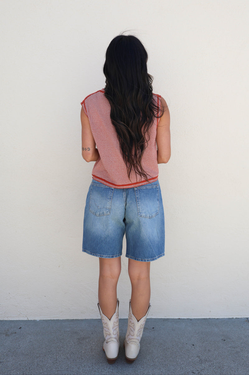 Person wearing a pink sleeveless top and denim shorts standing against a white wall.