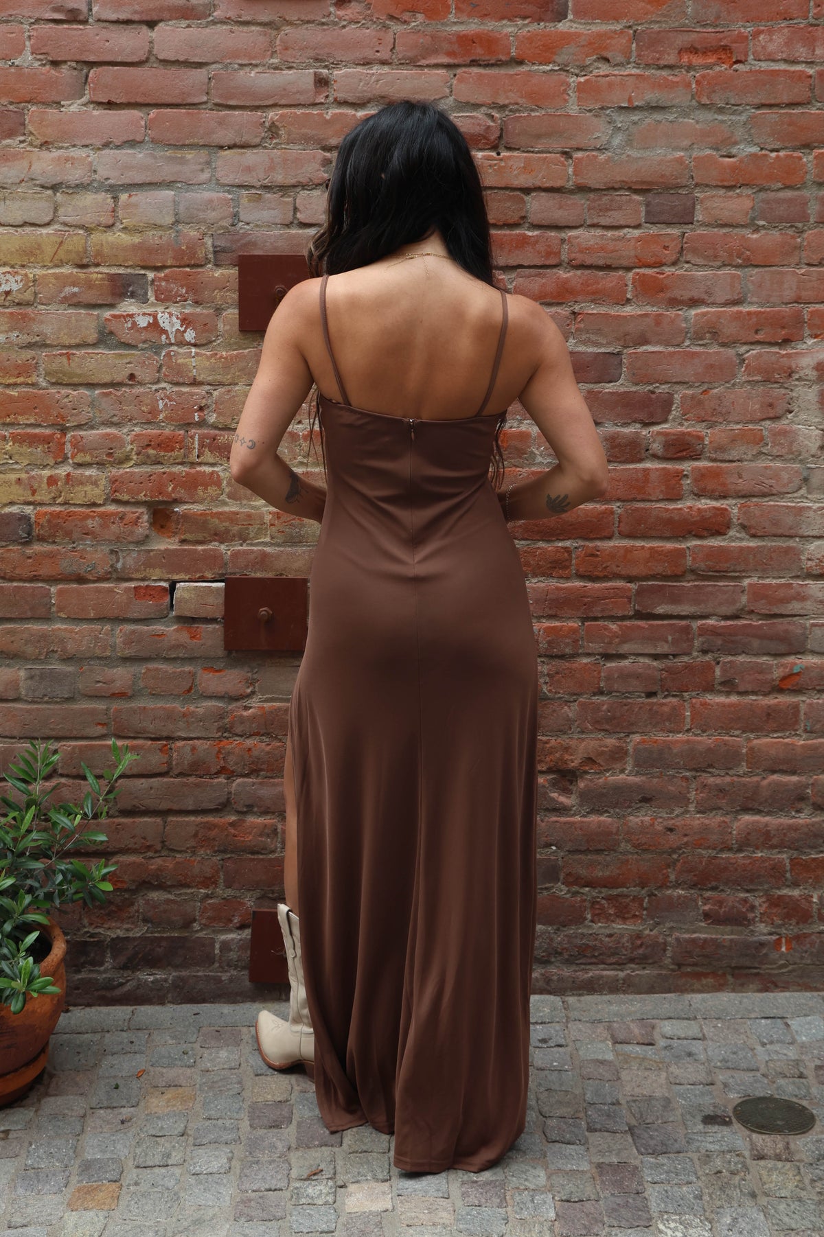 Woman in a brown dress standing against a brick wall