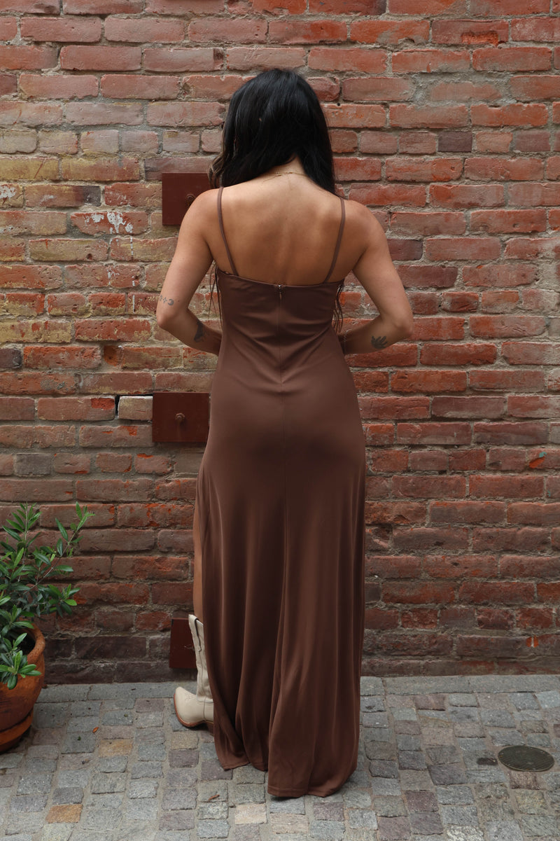 Woman in a brown dress standing against a brick wall