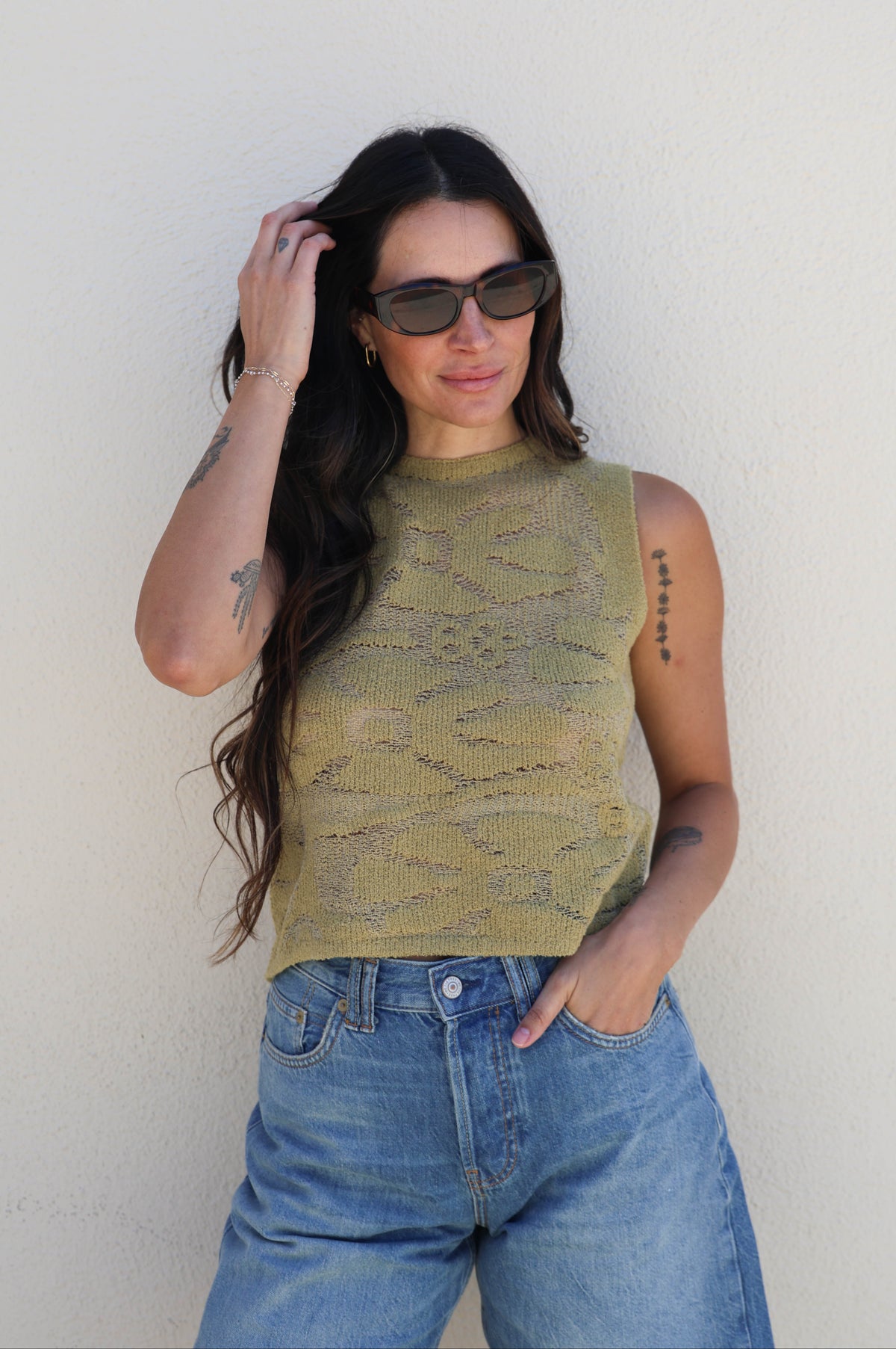 Woman wearing a green sleeveless top and blue jeans against a plain background