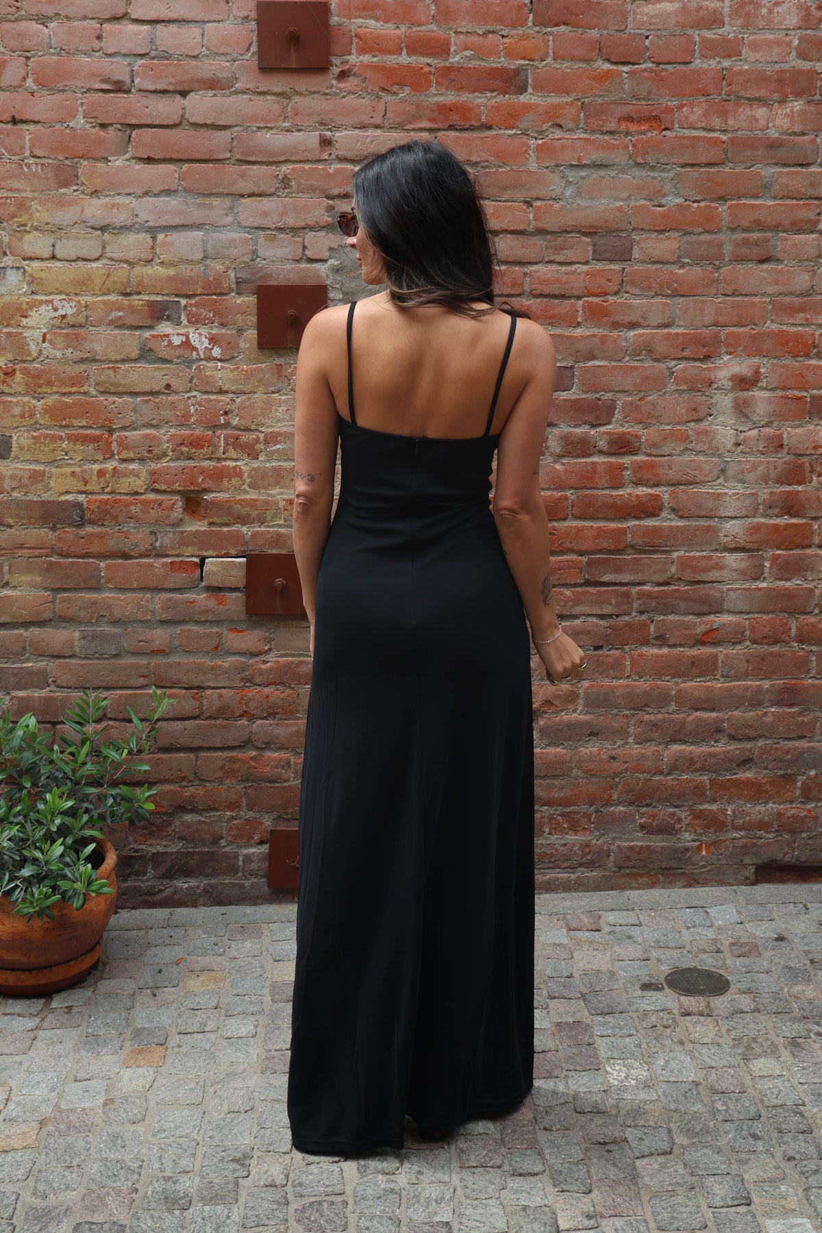 Woman in a black dress standing against a brick wall