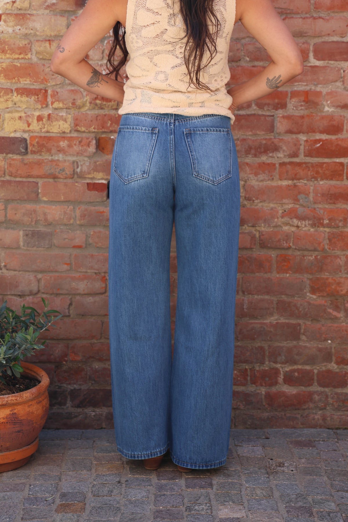 Person wearing blue jeans standing against a brick wall.
