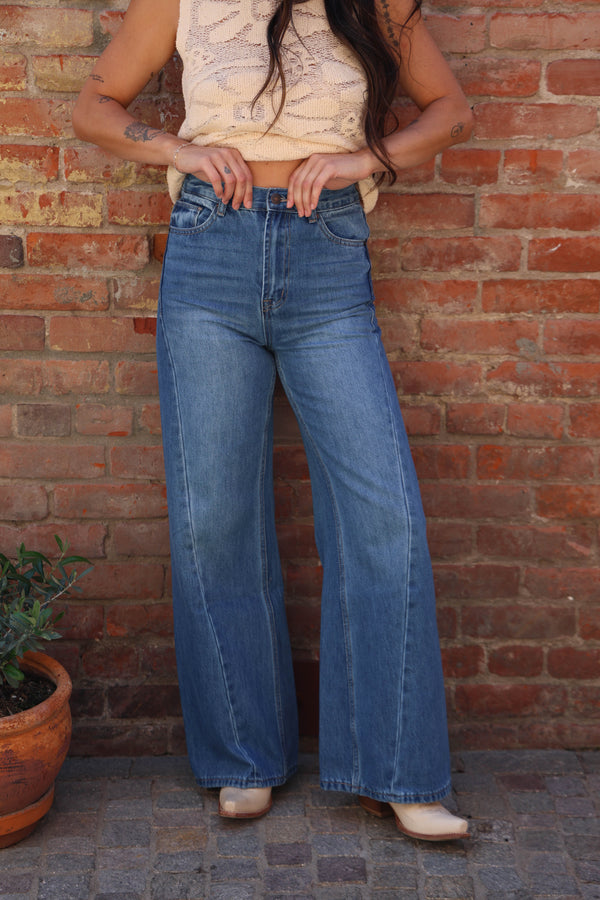 Person wearing blue jeans standing against a brick wall.