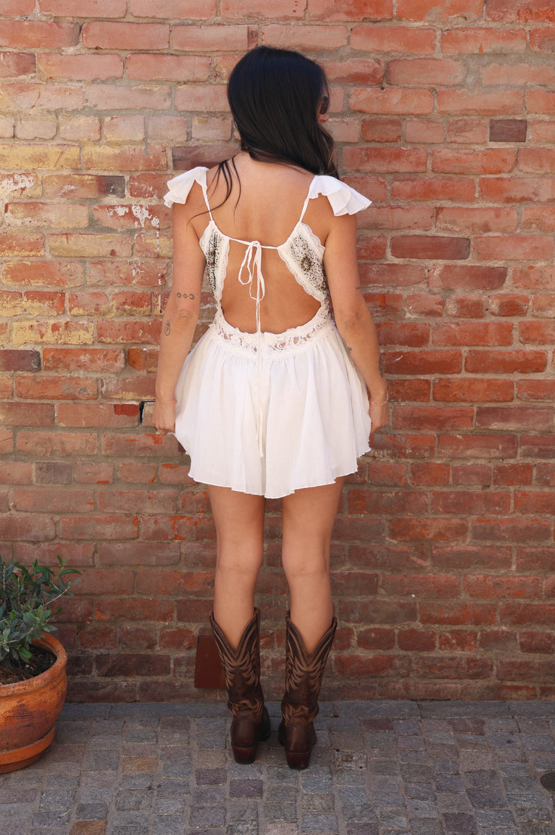 Person wearing a white dress with an open back and cowboy boots standing against a brick wall.