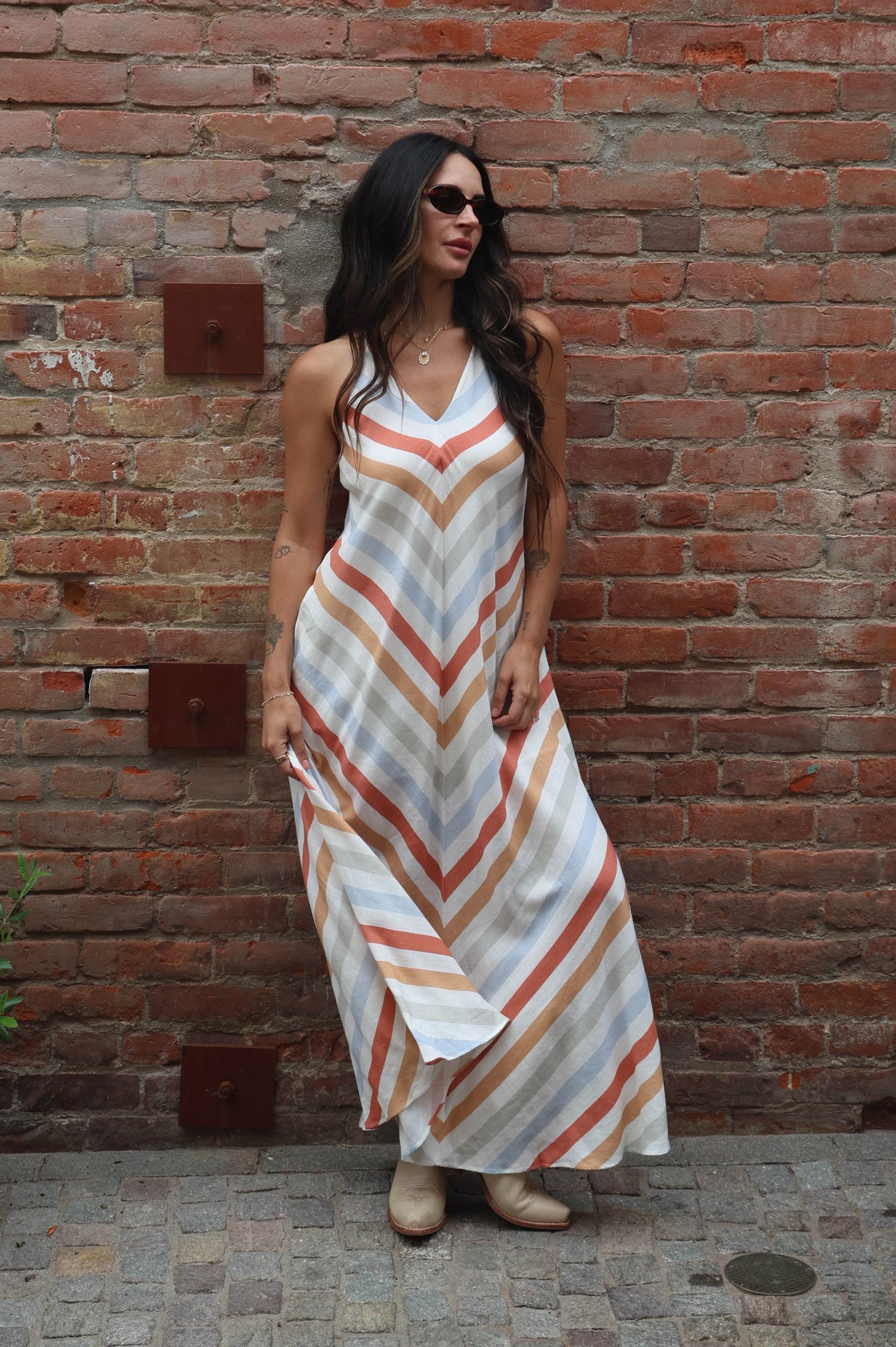 Woman in a striped dress standing against a brick wall.