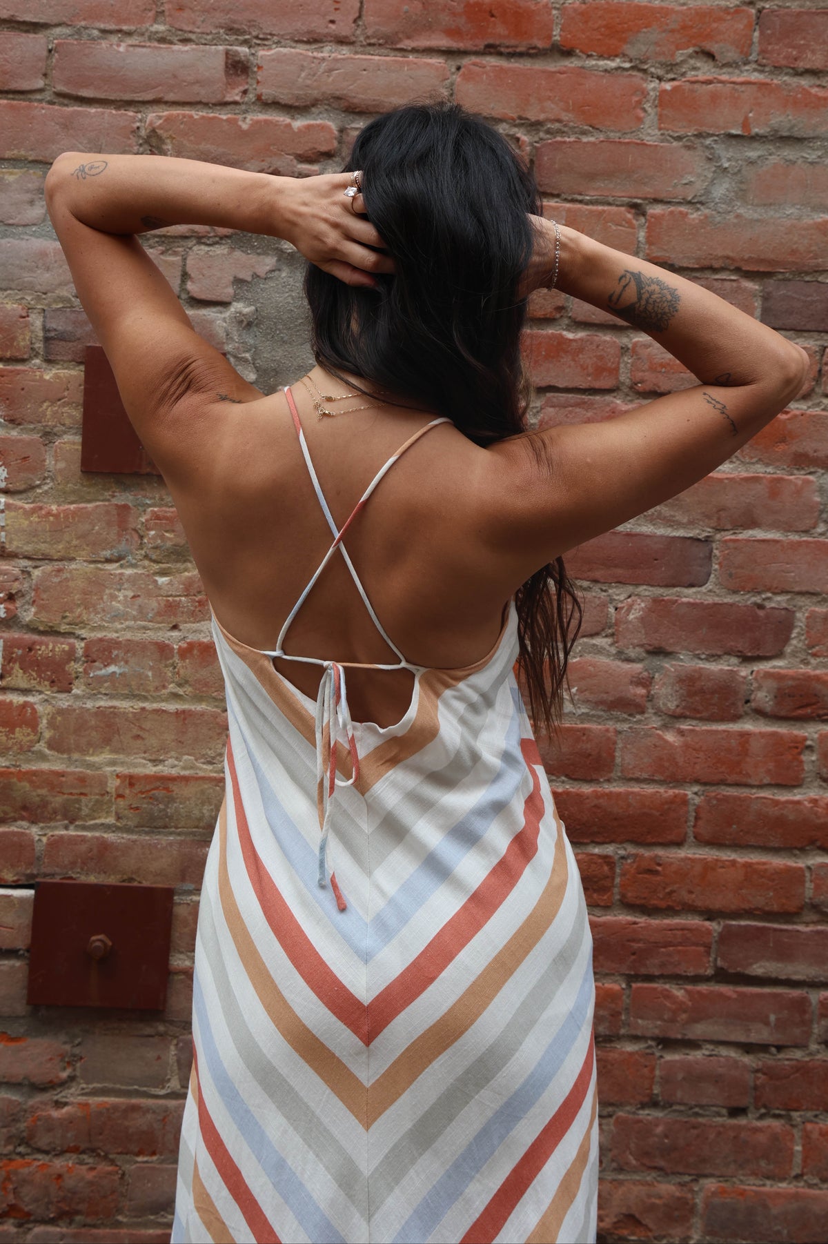 Woman in a striped dress standing against a brick wall