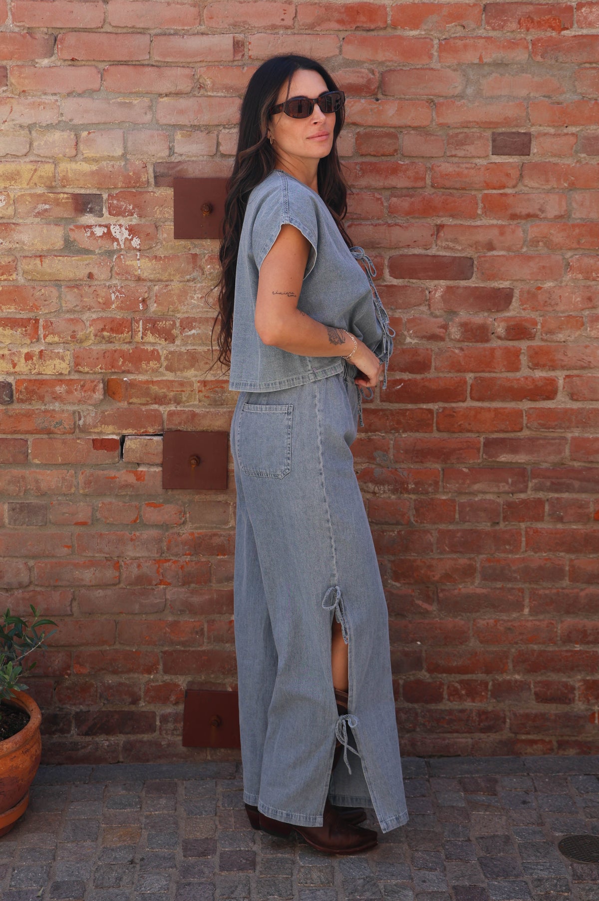 Woman in a gray outfit standing against a brick wall