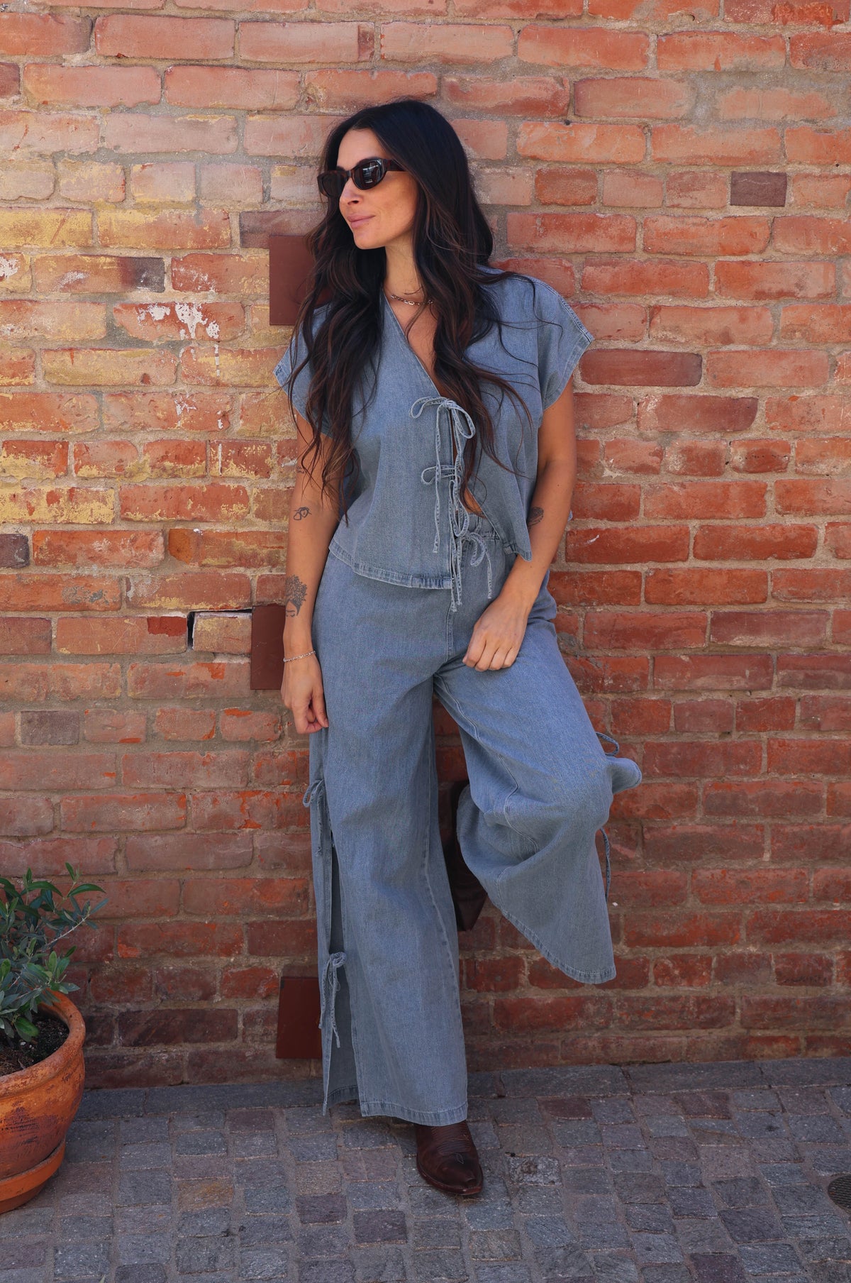 Woman in a denim outfit standing against a brick wall