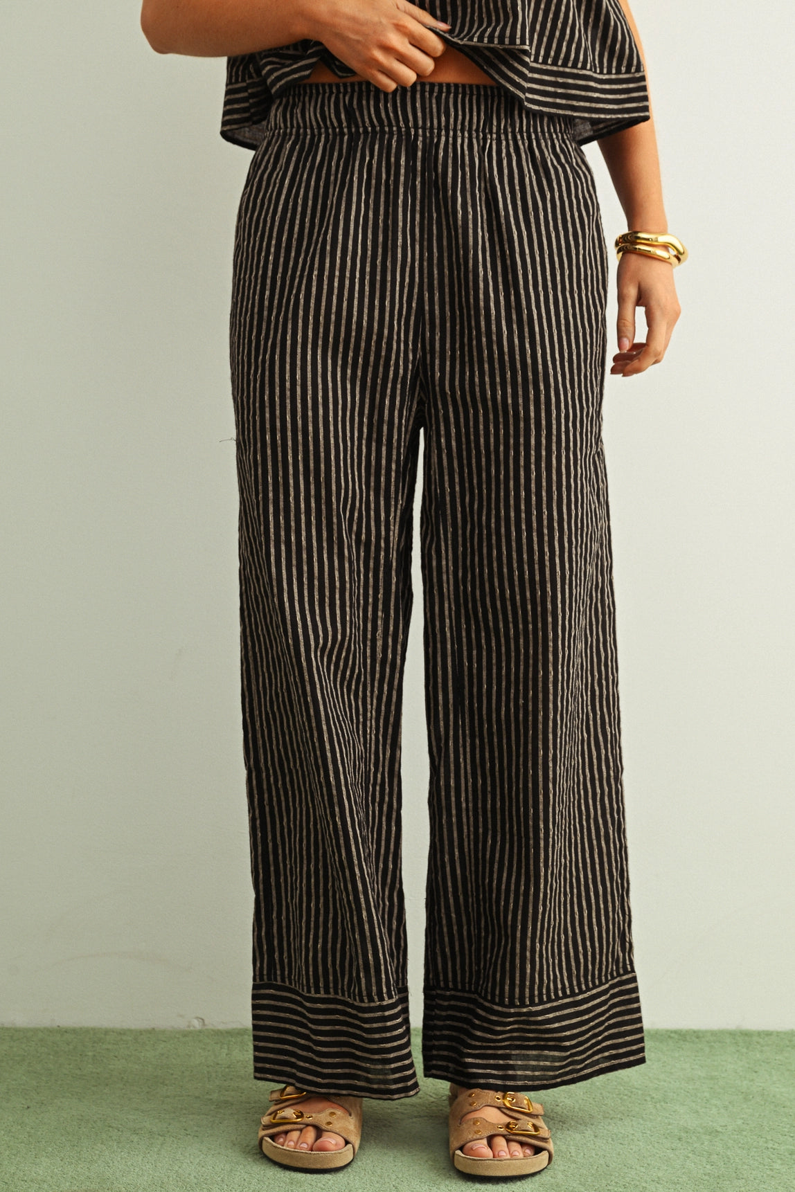 Person wearing striped pants and sandals on a plain background