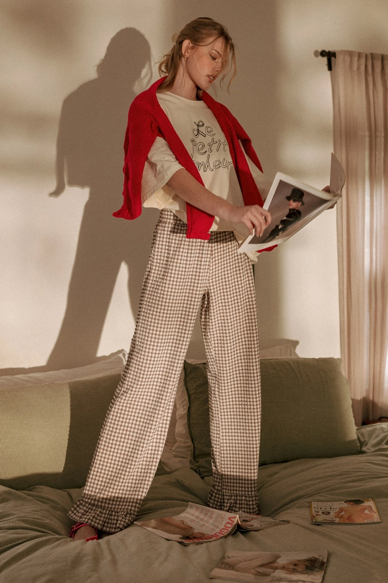 Woman in a red cardigan and checkered pants holding a magazine on a bed.
