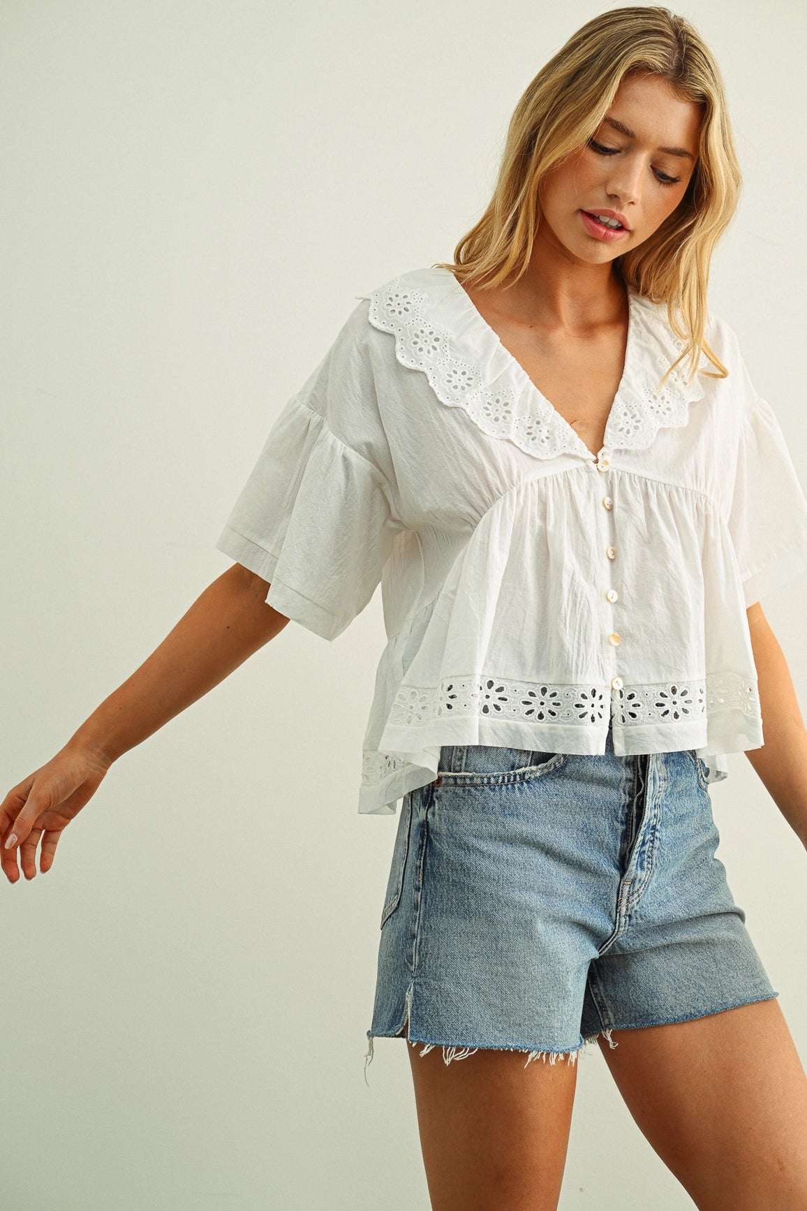 Woman wearing a white blouse with lace details and denim shorts on a plain background