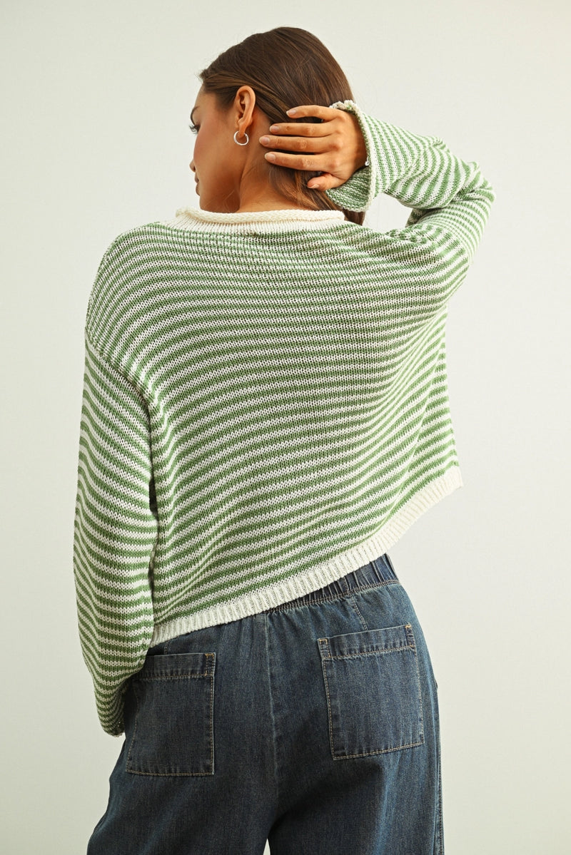 Person wearing a green and white striped sweater and blue jeans against a plain background
