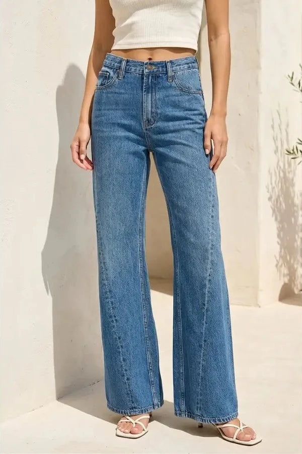 Person wearing blue wide-leg jeans and a white top against a neutral background