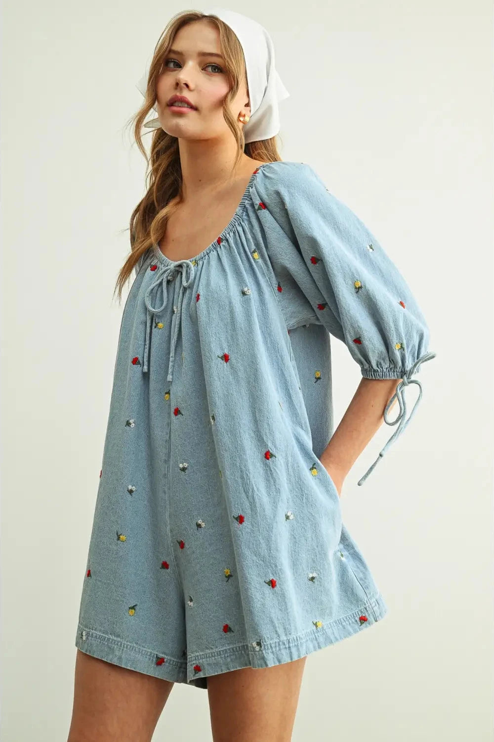 Woman wearing a light blue denim dress with colorful embroidery on a plain background