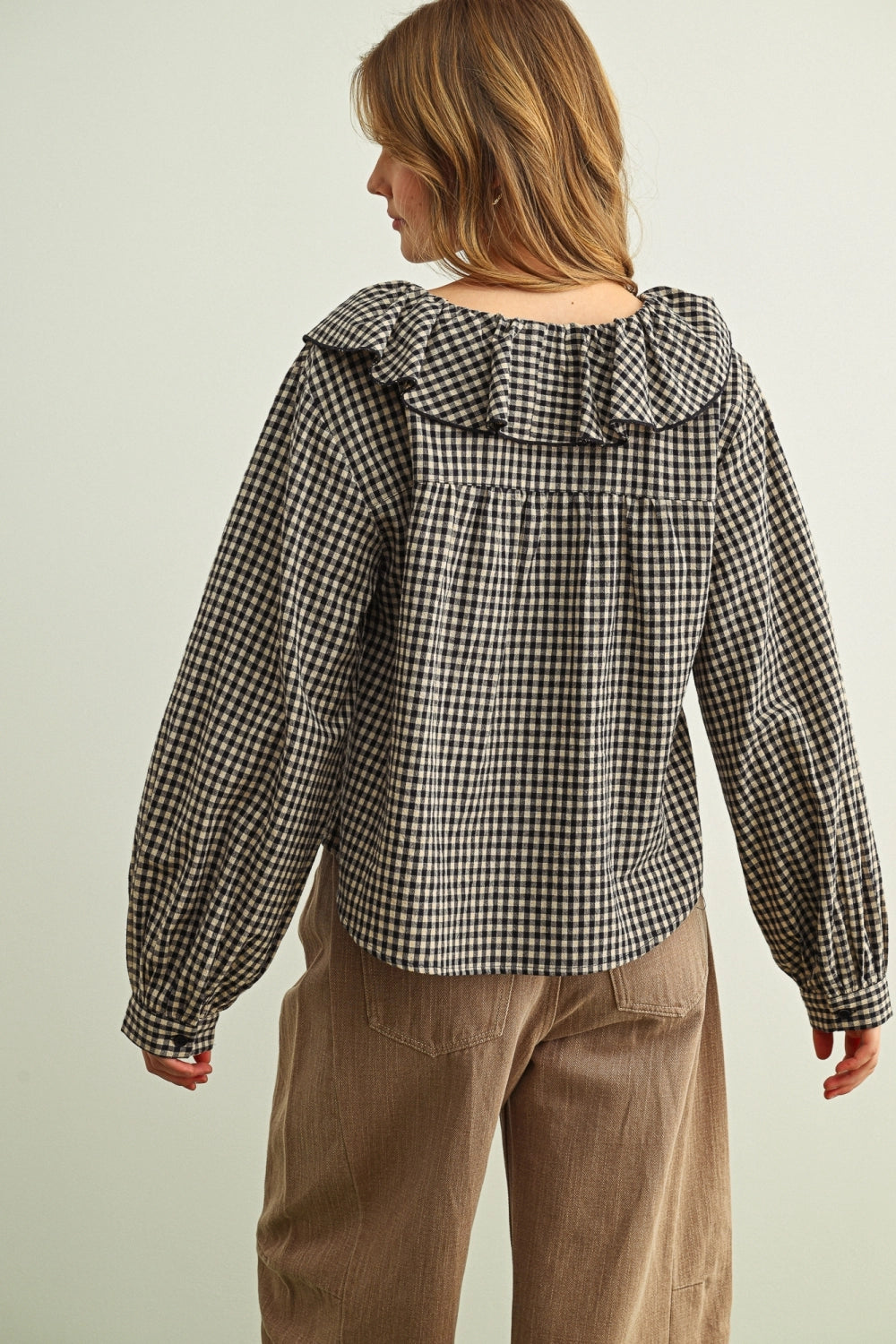 Person wearing a black and white checkered blouse with ruffled shoulders on a plain background