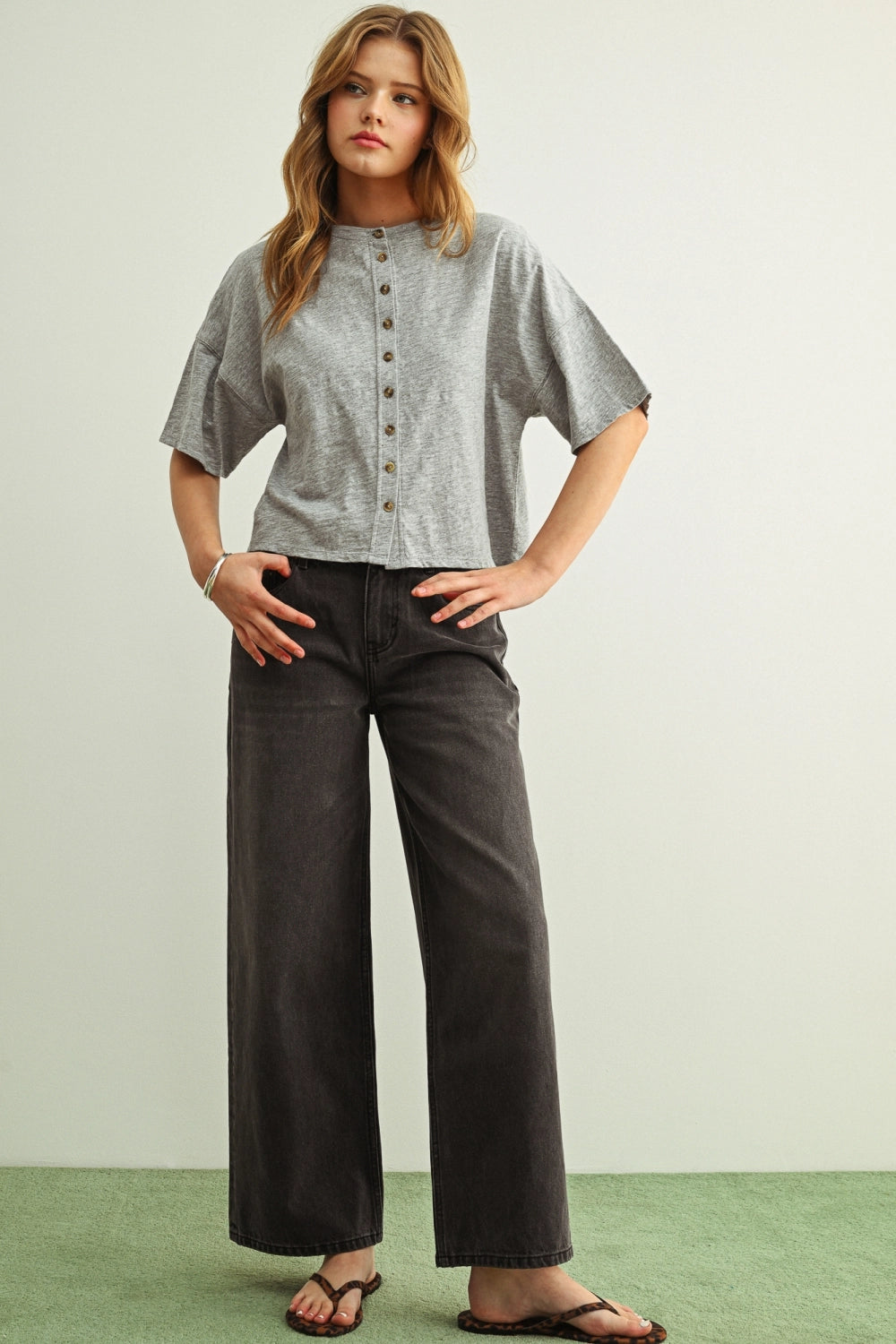 Woman wearing a grey shirt with buttons against a white background.