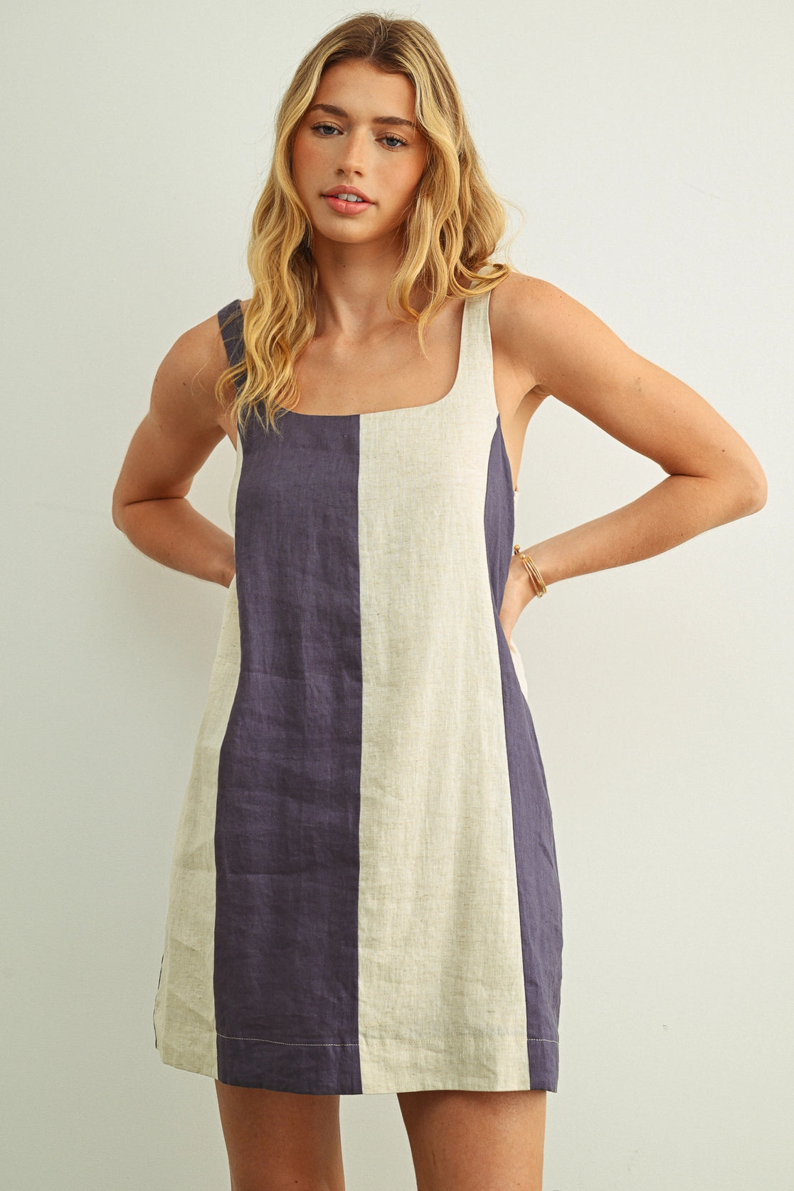Woman wearing a sleeveless dress with purple and white color block design on a plain background