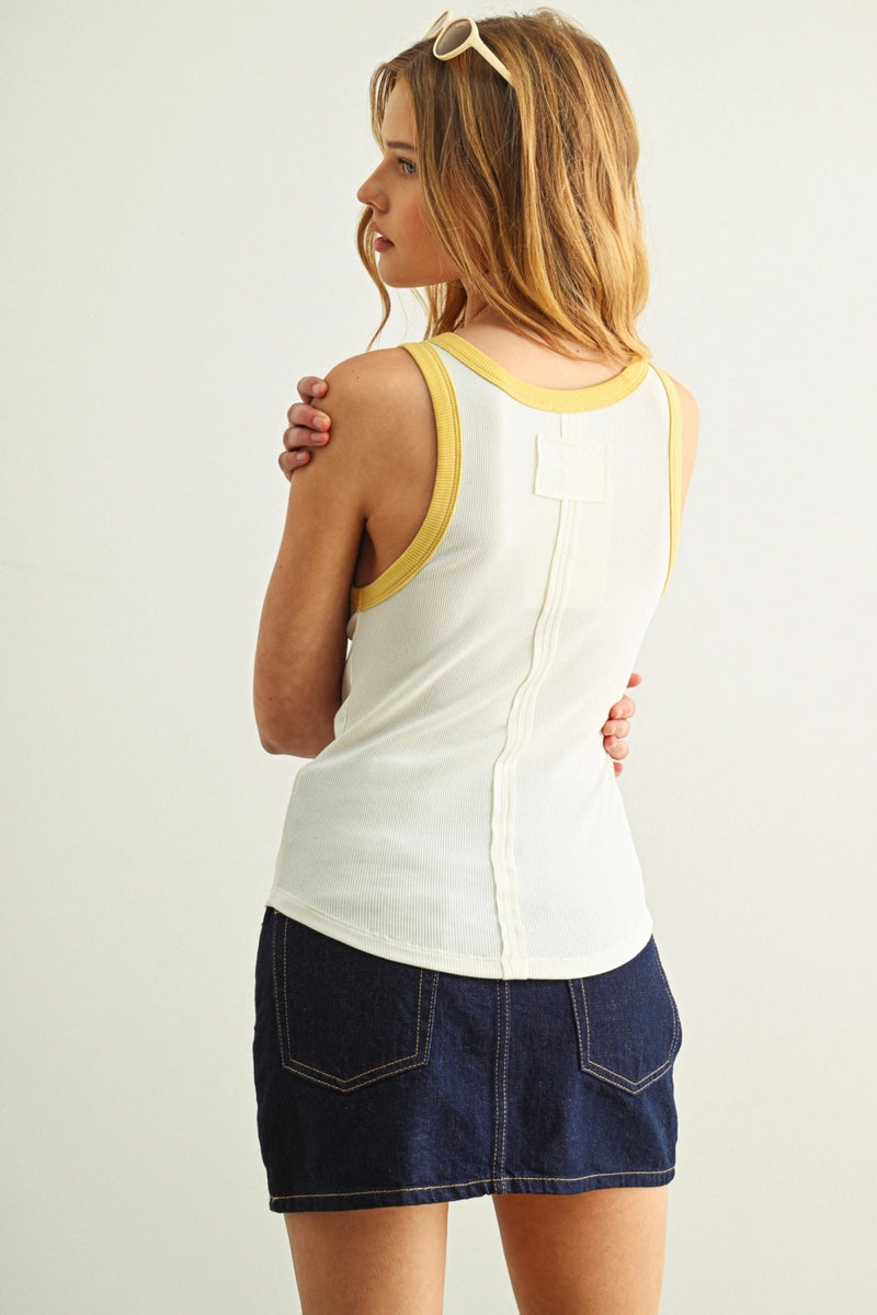 Woman wearing a white tank top with yellow trim and a denim skirt on a plain background