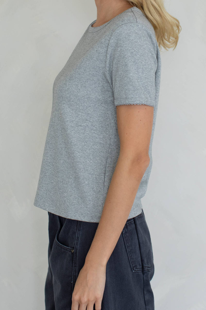 Person wearing a gray t-shirt and dark pants against a plain background