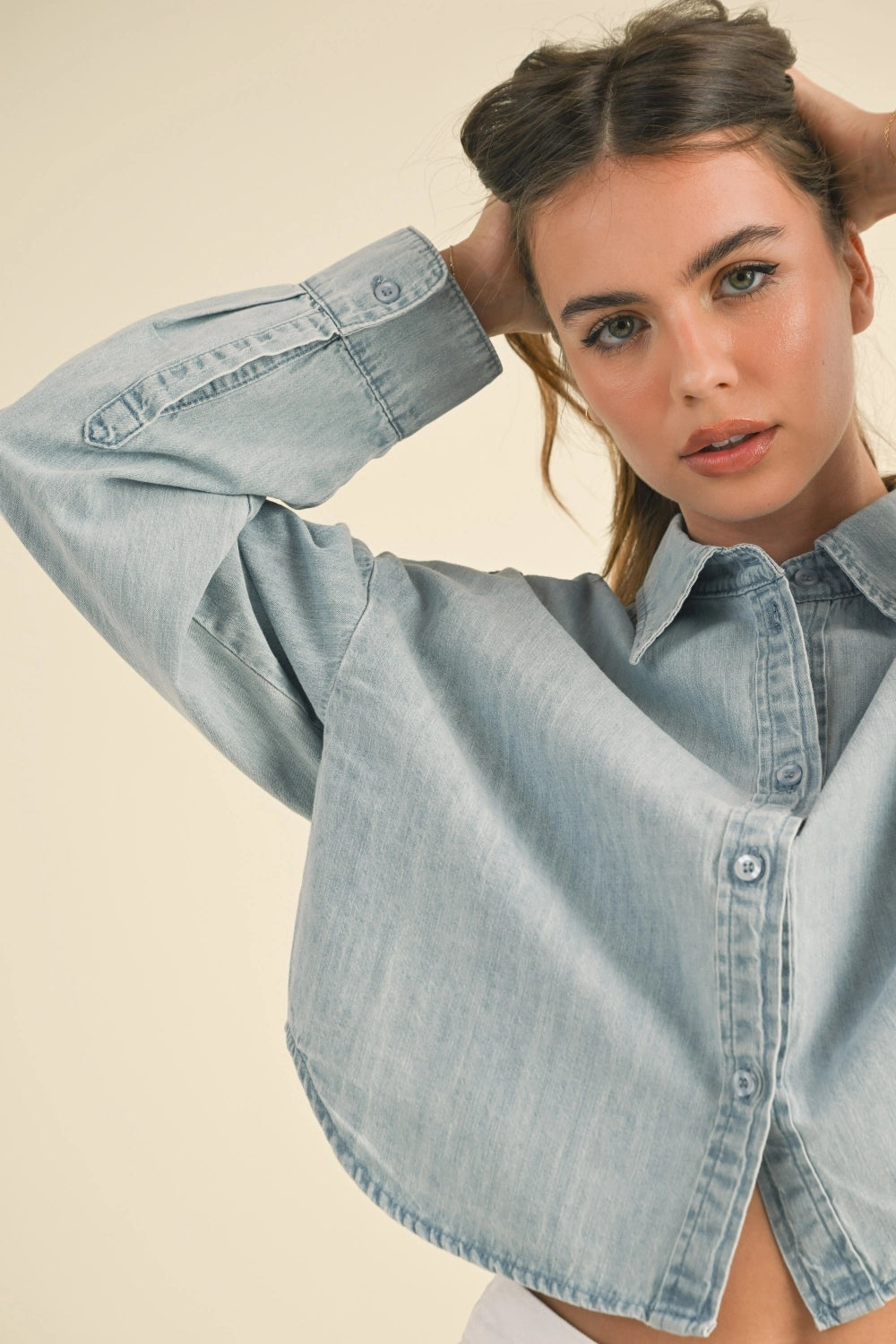 Woman wearing a light blue denim shirt against a beige background