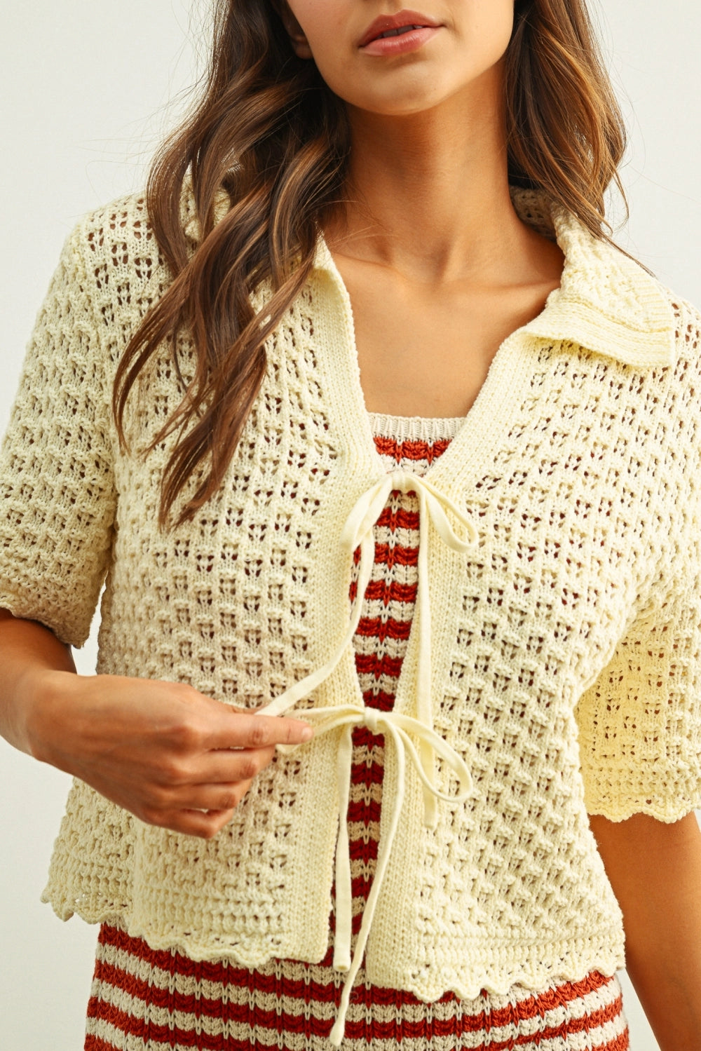 Woman wearing a cream-colored crochet cardigan over a striped dress.